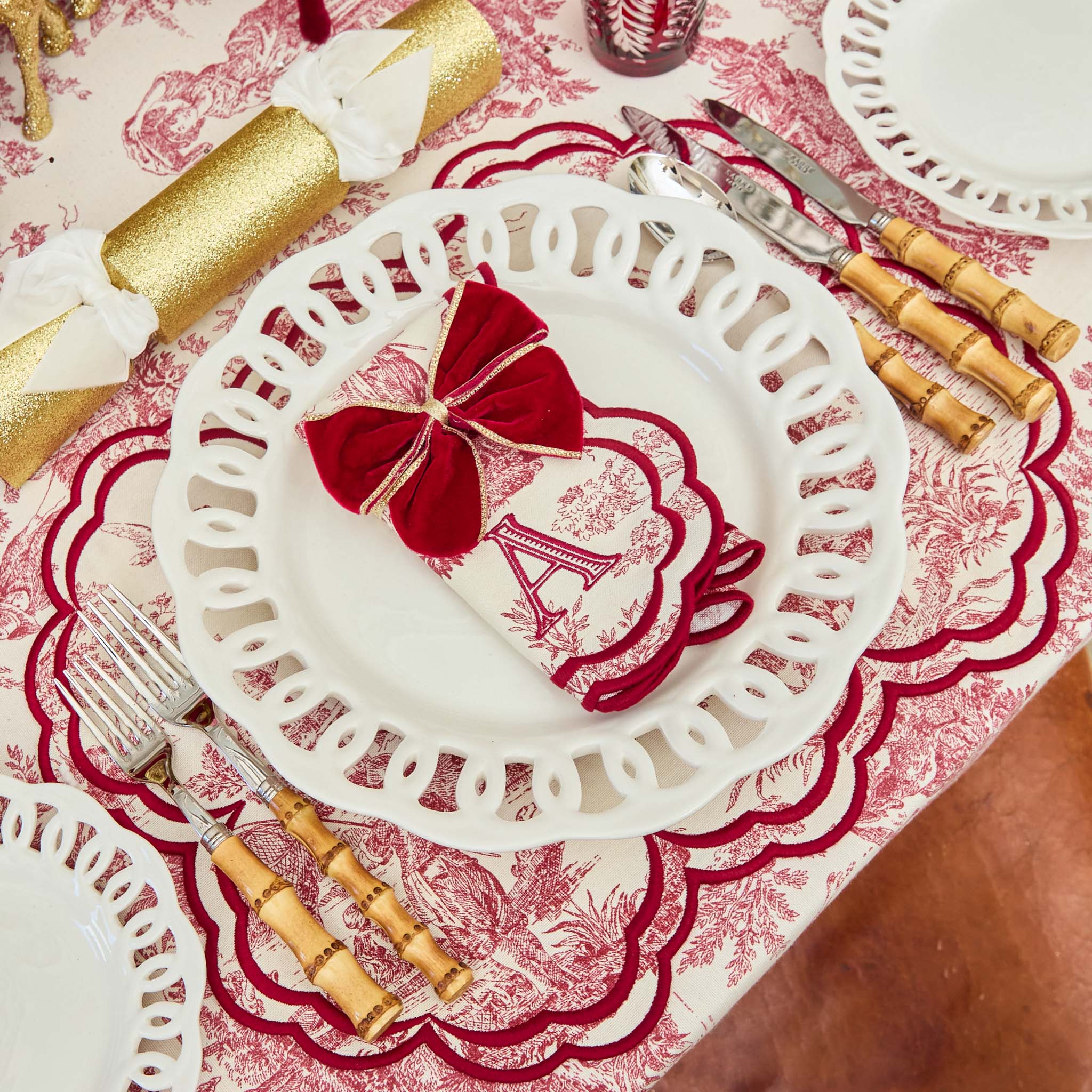 Decorative table setting with a red and white patterned plate featuring the Eiffel Tower, surrounded by gold and wooden cutlery on a matching tablecloth.