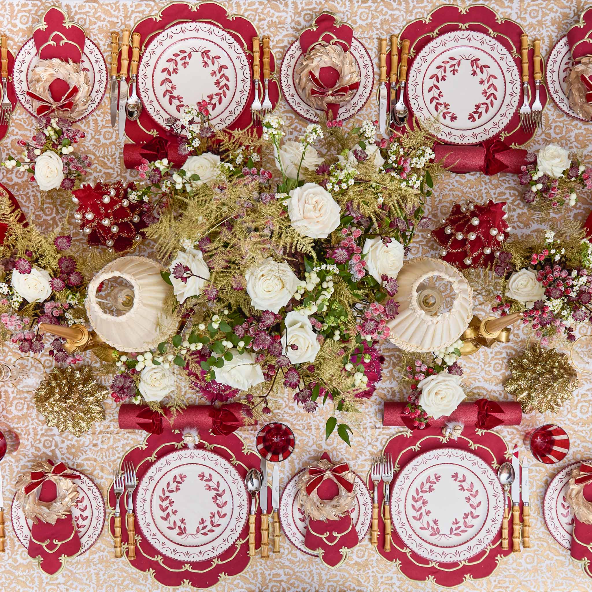 Decorative table setting with red and white plates, flowers, and gold accents on a patterned tablecloth.