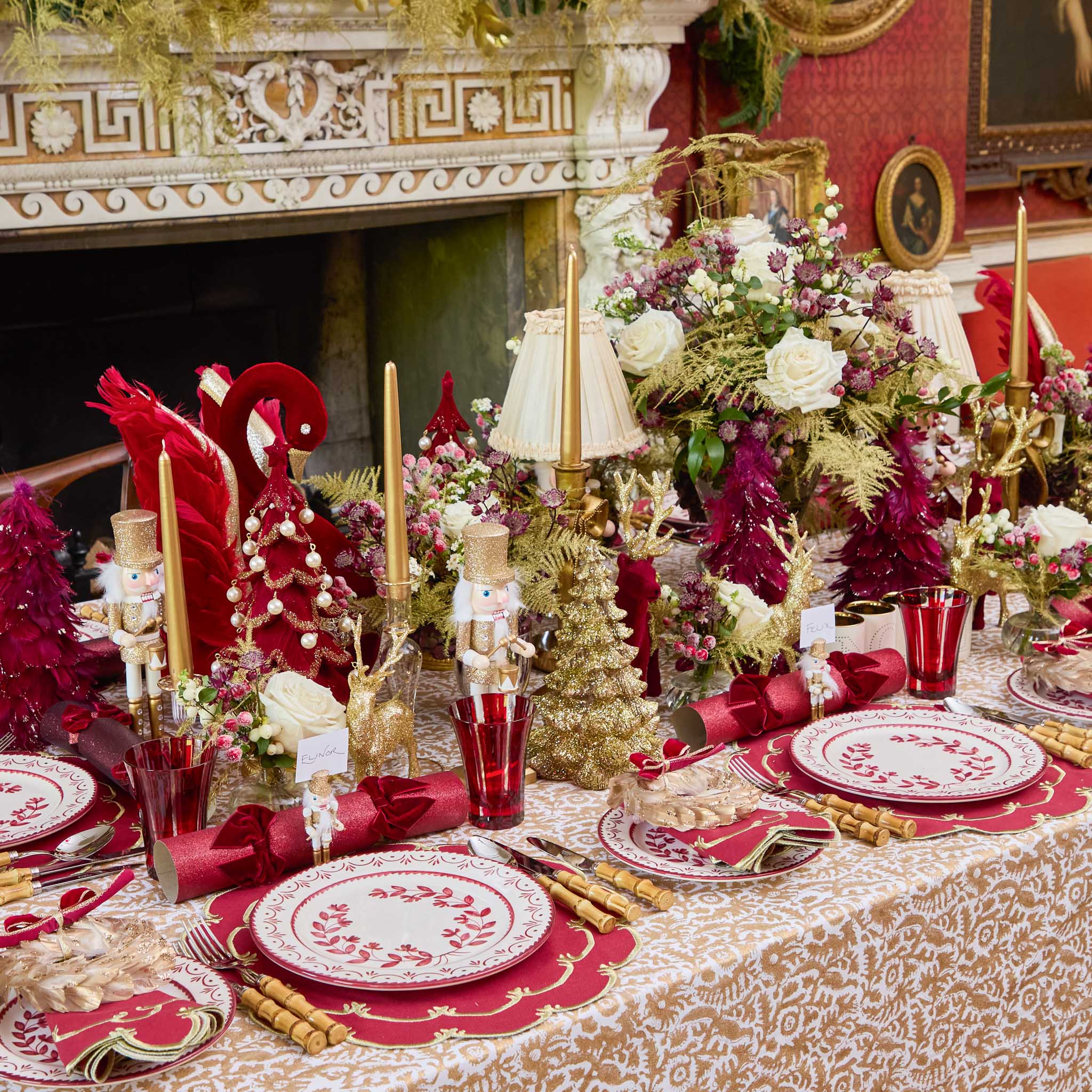 Decorative Christmas table setting with red and gold accents, including plates, napkins, and candles.