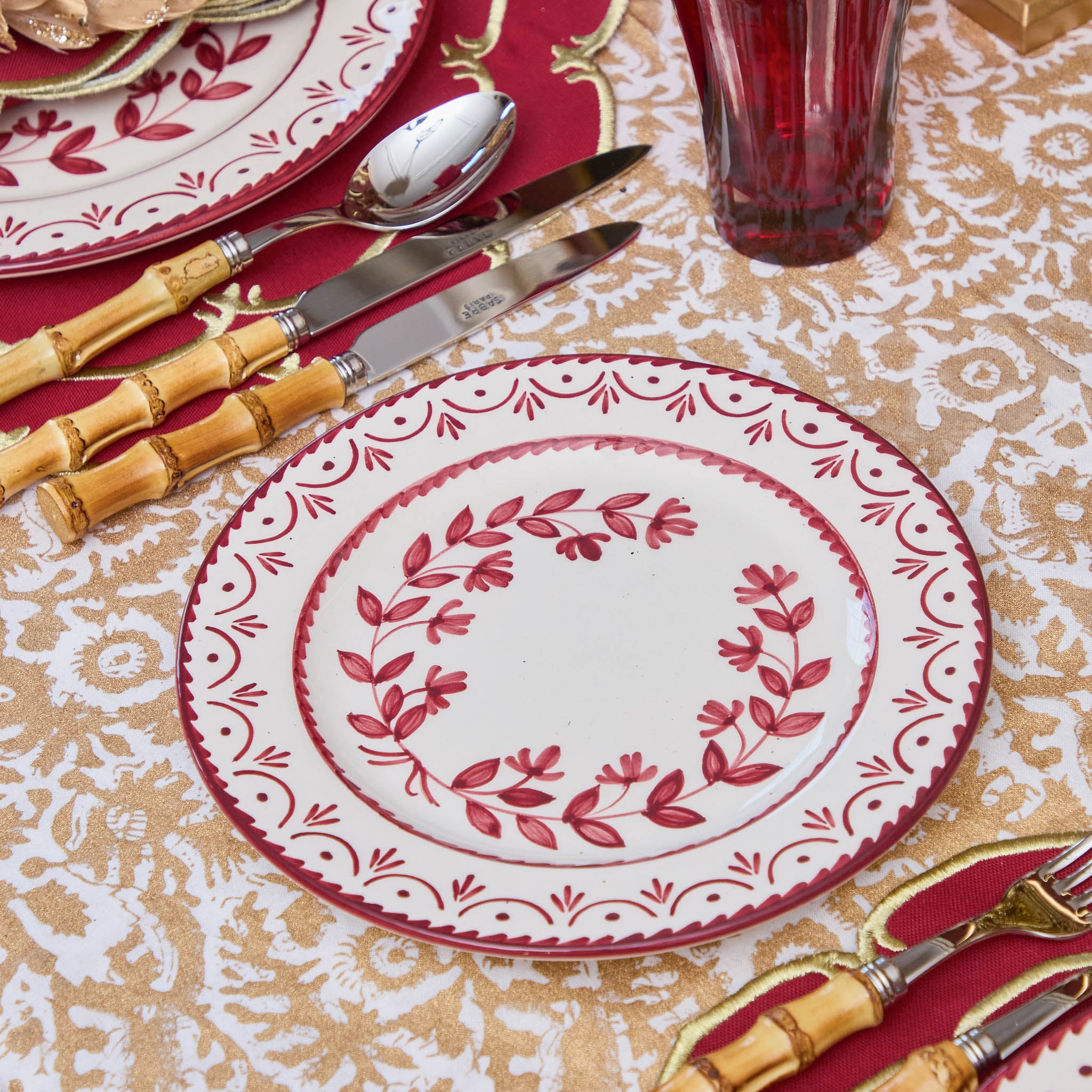 Decorative table setting with red and white plates, silverware, and a patterned tablecloth.