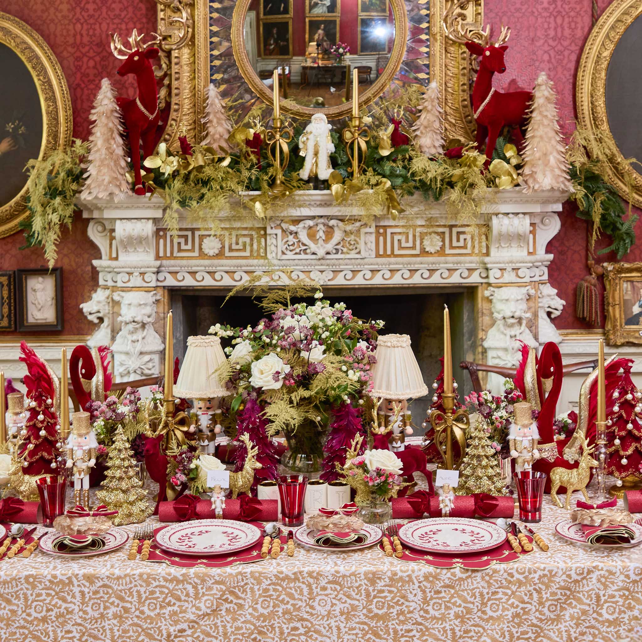 Decorative xmas table setting with floral centerpieces, red and gold tableware, and festive decorations in a richly decorated room.