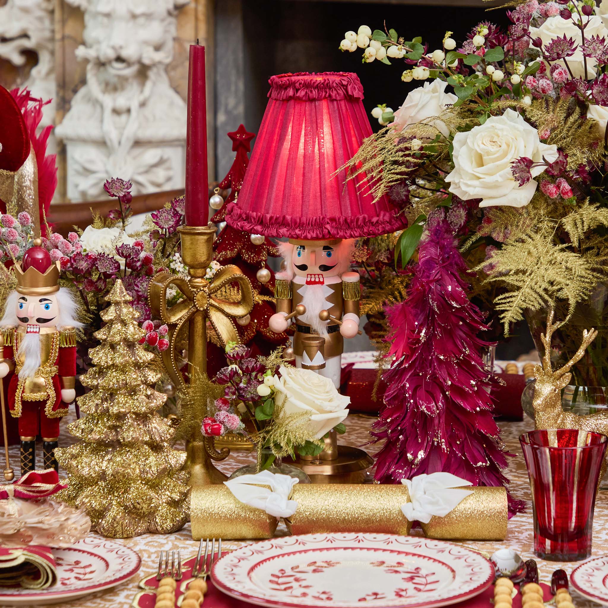 Decorative Christmas table setting with red and gold elements, including a lampshade and trees.