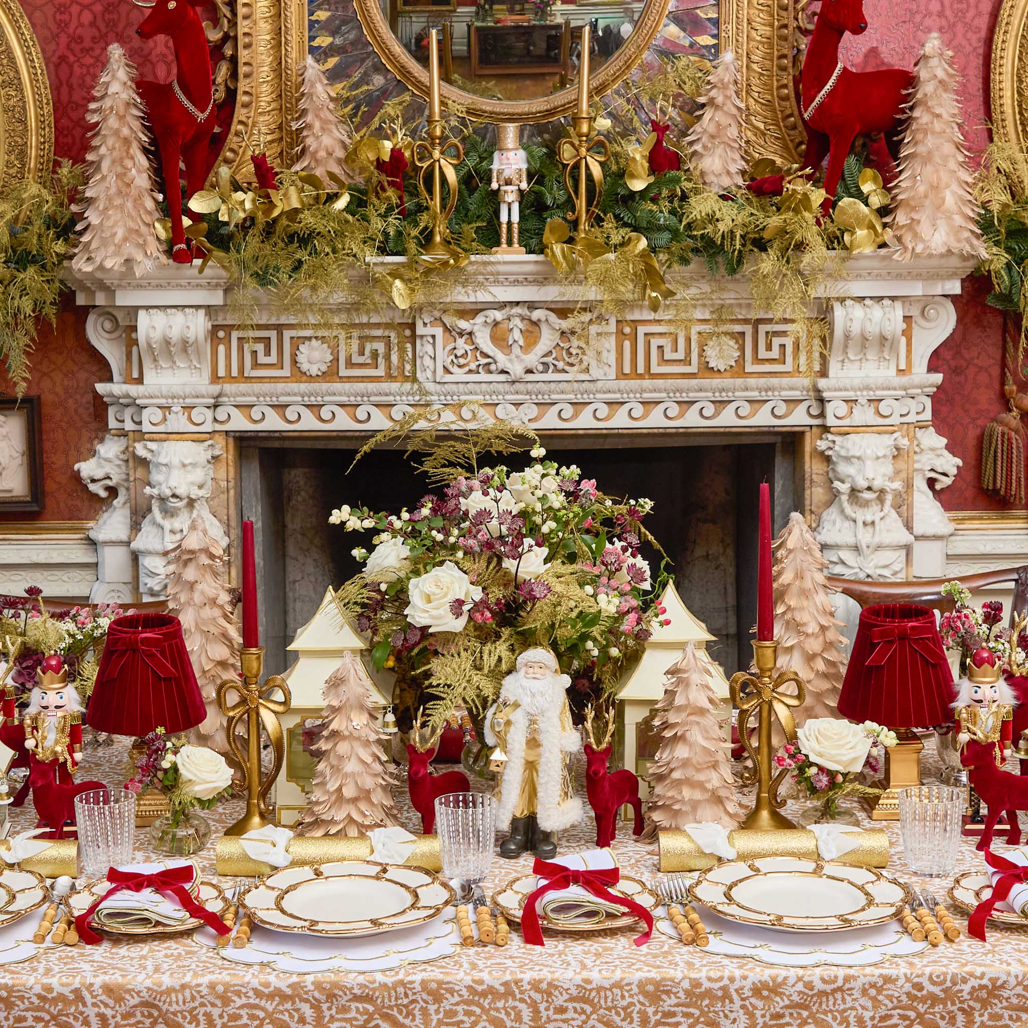 Decorative Christmas table setting with gold, red, and white elements in front of a fireplace.