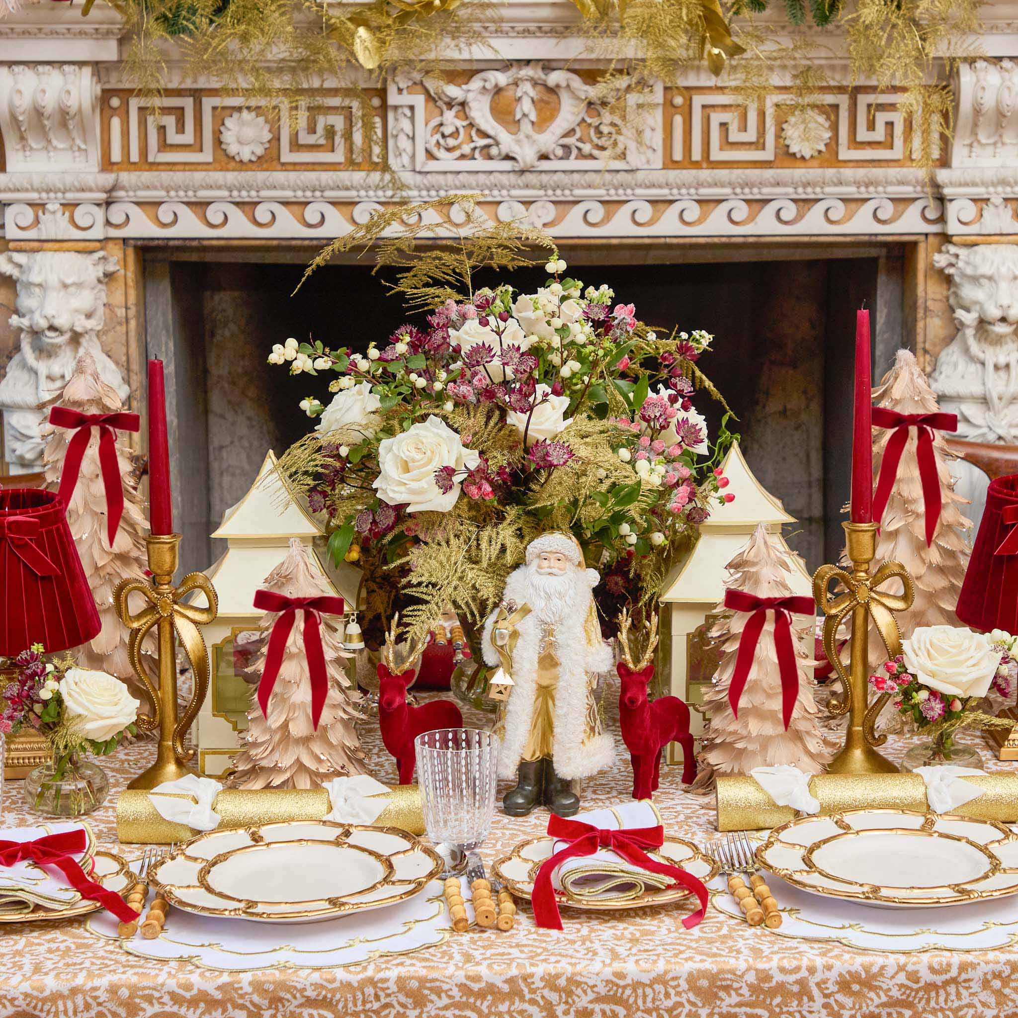 Decorative Christmas table setting with Santa Claus figure, candles, and floral arrangements.
