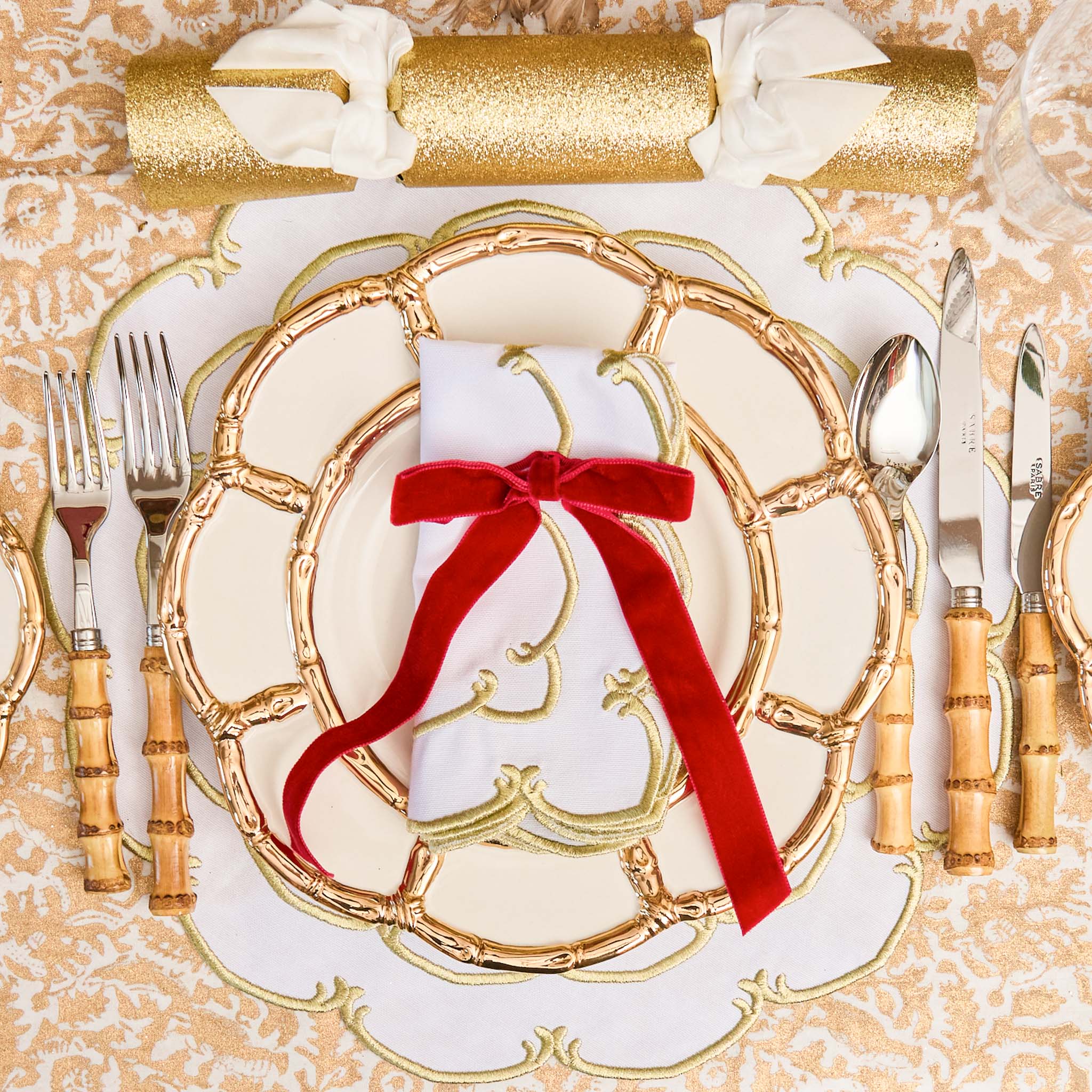 Decorative table setting with gold plates, silverware, and a red ribbon on a textured surface.