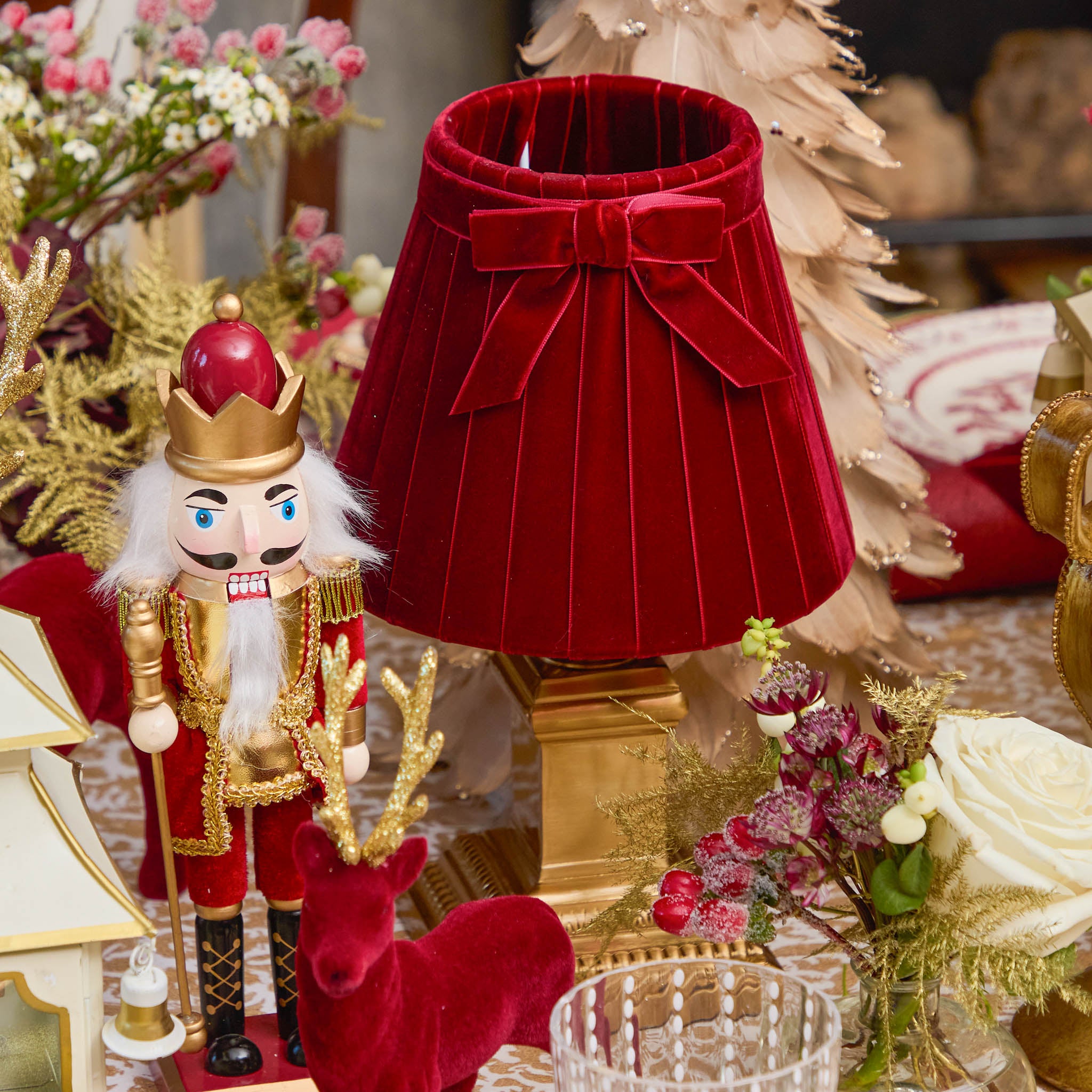 Decorative red lampshade with a bow, nutcracker figure, and reindeer in a festive setting.