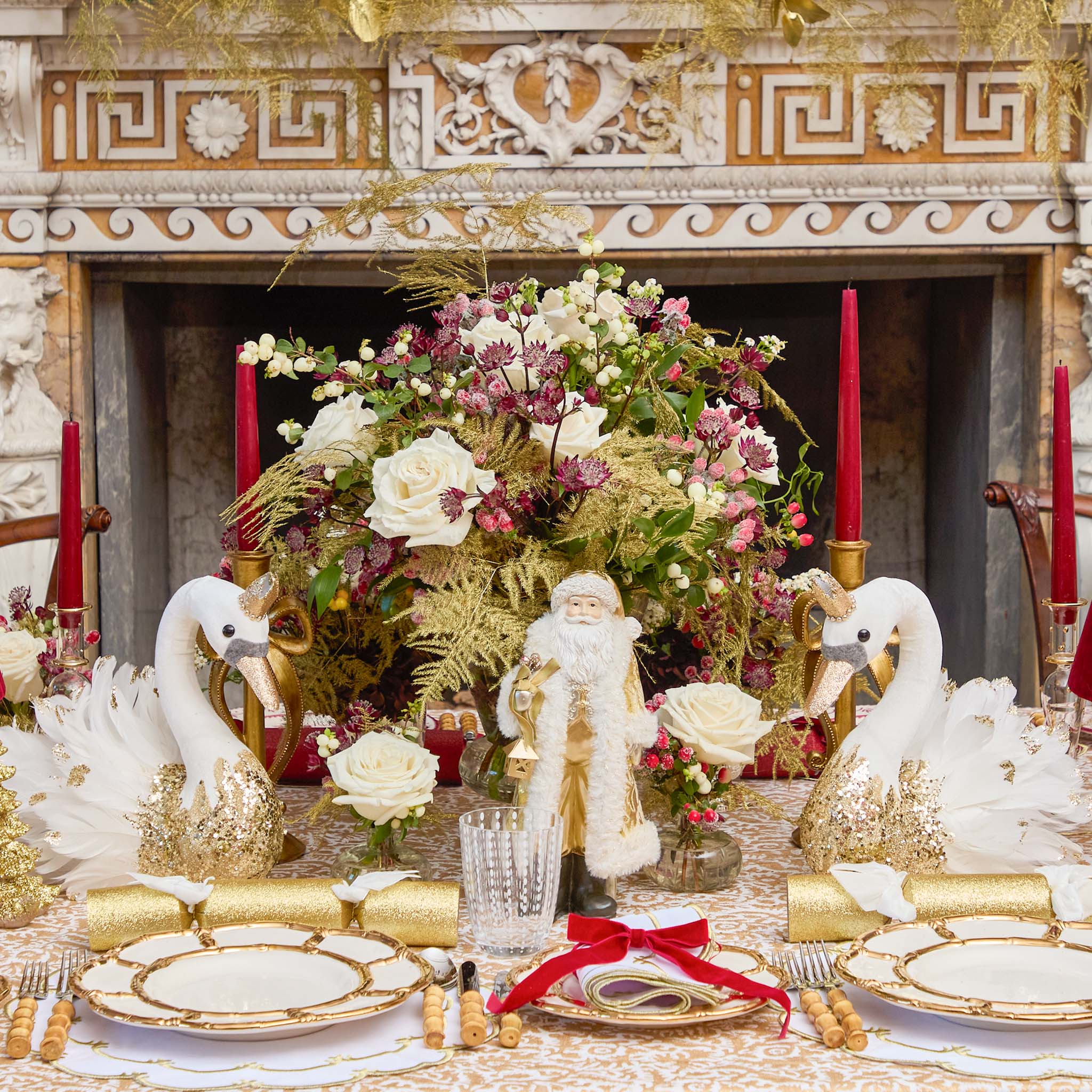 Decorative Christmas table setting with floral arrangement, Santa figurine, and swan decorations in front of a fireplace.