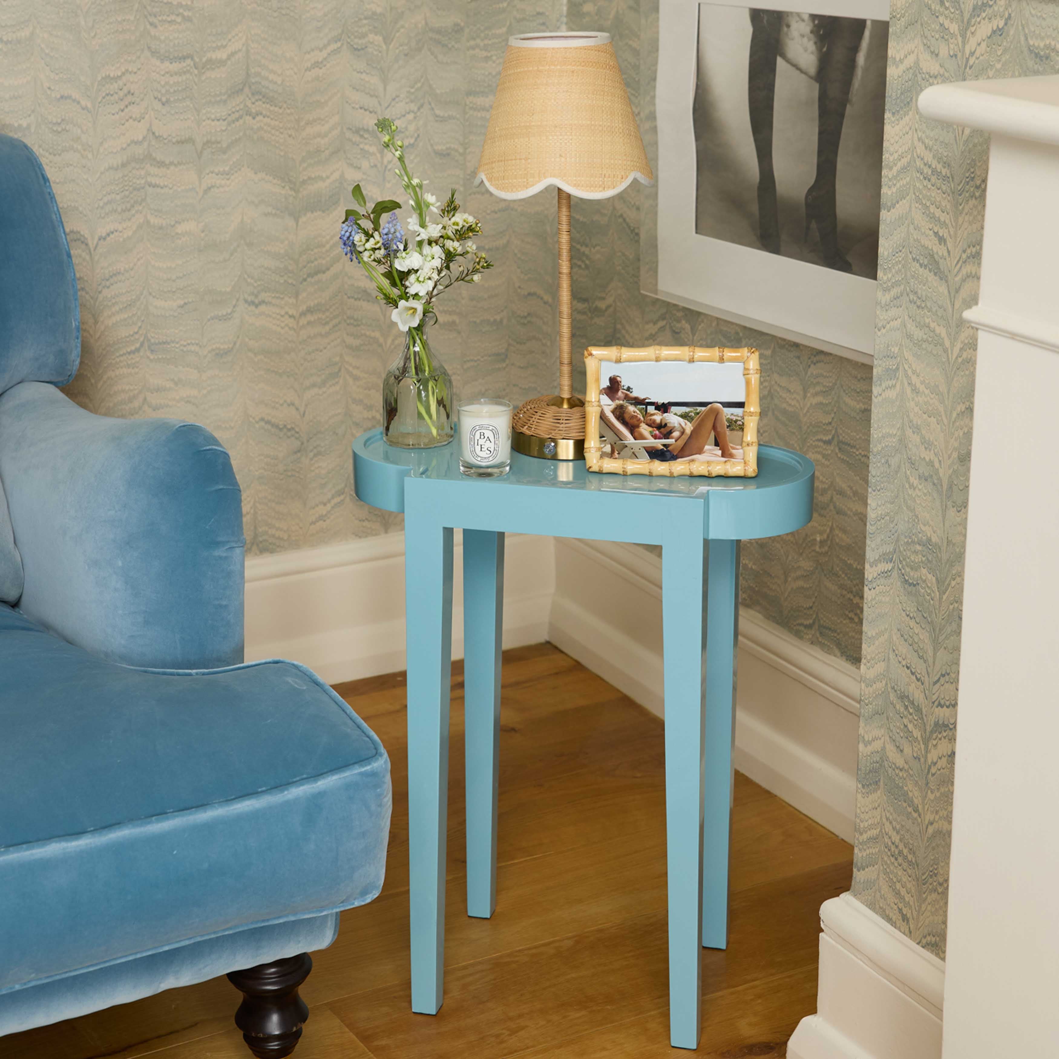 Blue side table with a lamp, candle, and picture frame next to a blue armchair.