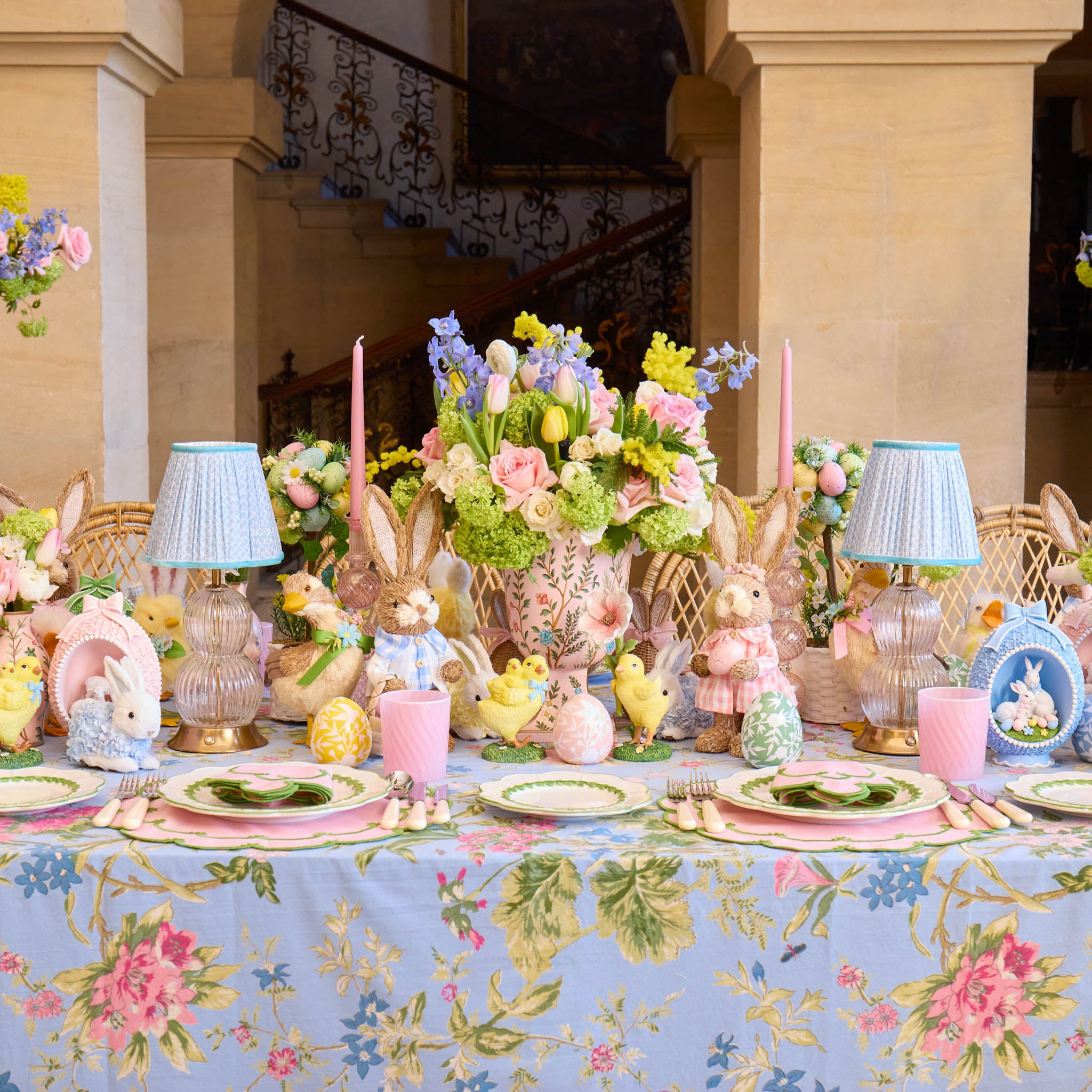 Easter-themed table setting with floral tablecloth, bunny decorations, and colorful tableware.