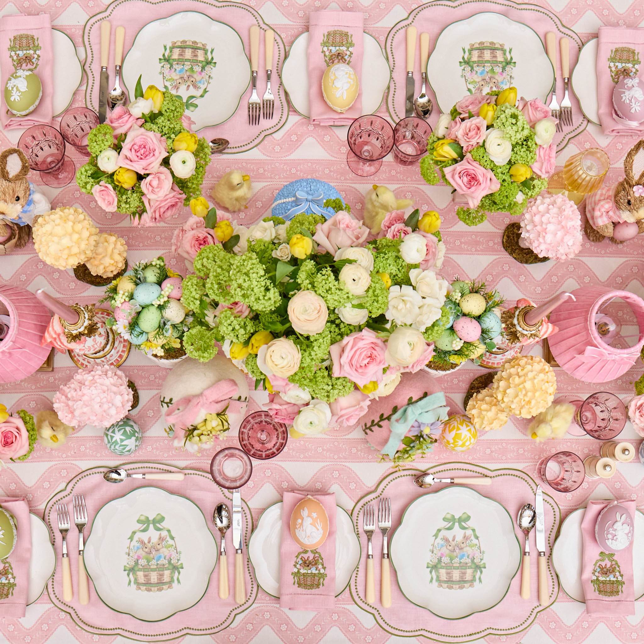 Decorative table setting with floral arrangements, plates, and cutlery on a pink patterned tablecloth.