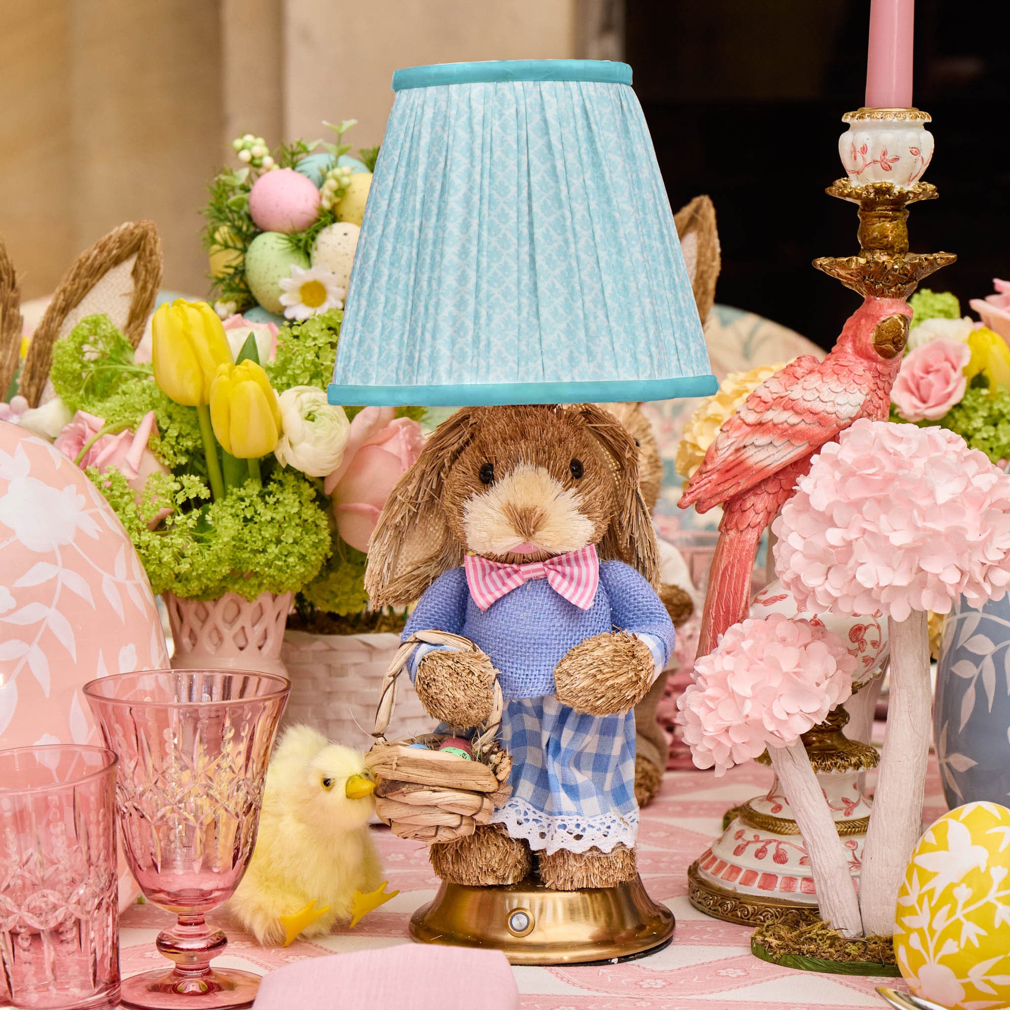 Decorative scene with a rabbit figurine holding a basket, surrounded by flowers and pastel-colored items.