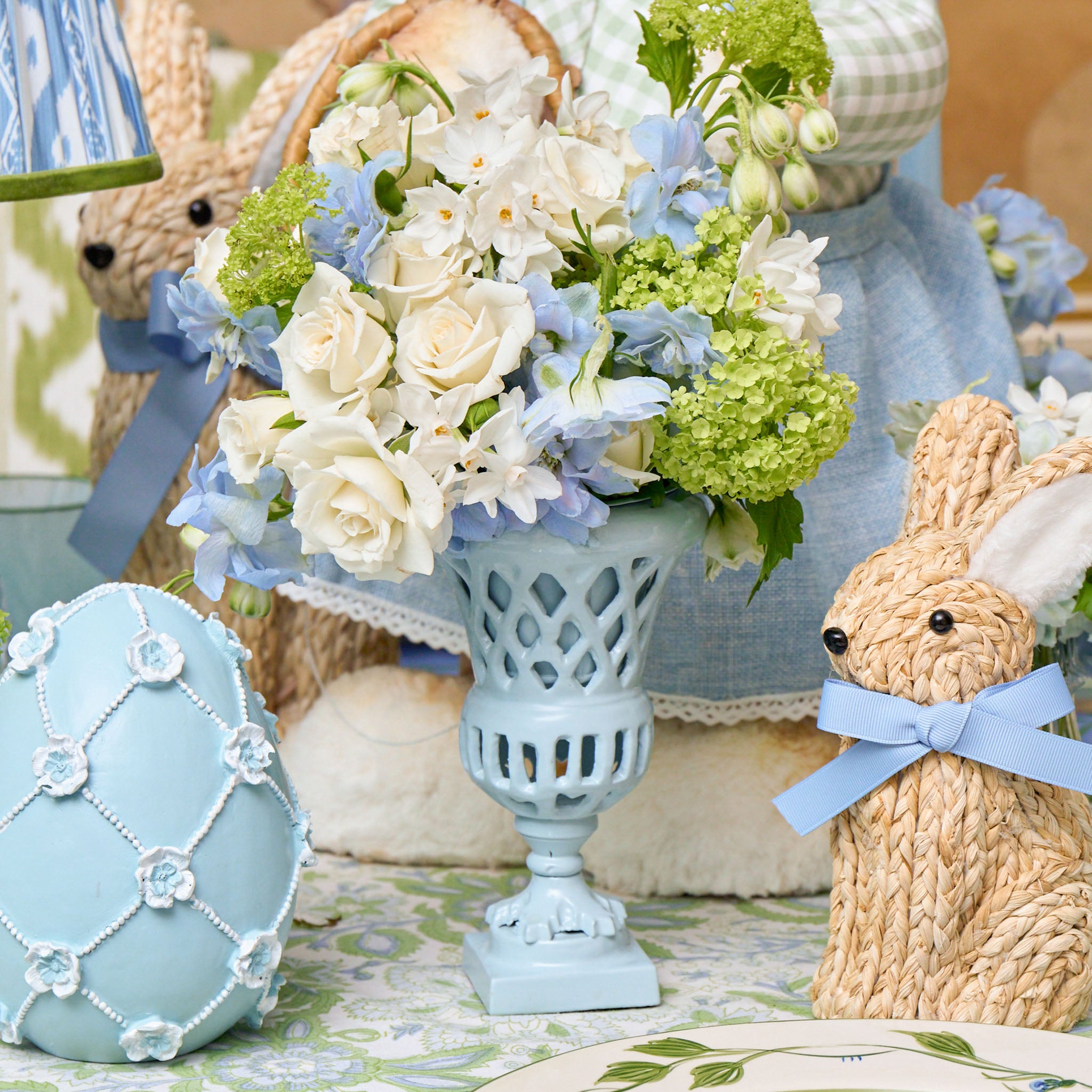 Decorative Easter scene with flowers, eggs, and bunnies on a floral tablecloth.