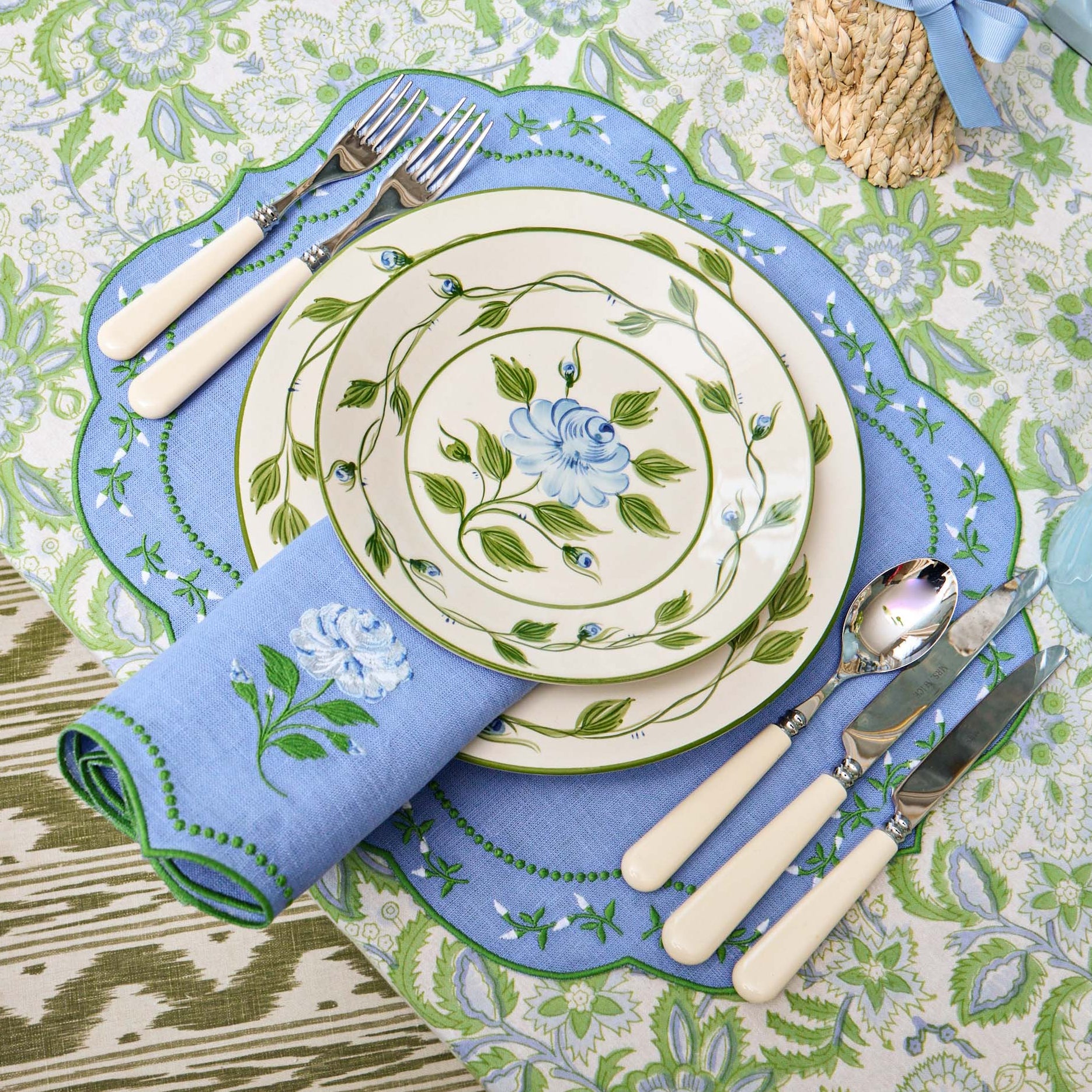 Decorative table setting with floral plates, cutlery, and napkins on a patterned tablecloth.