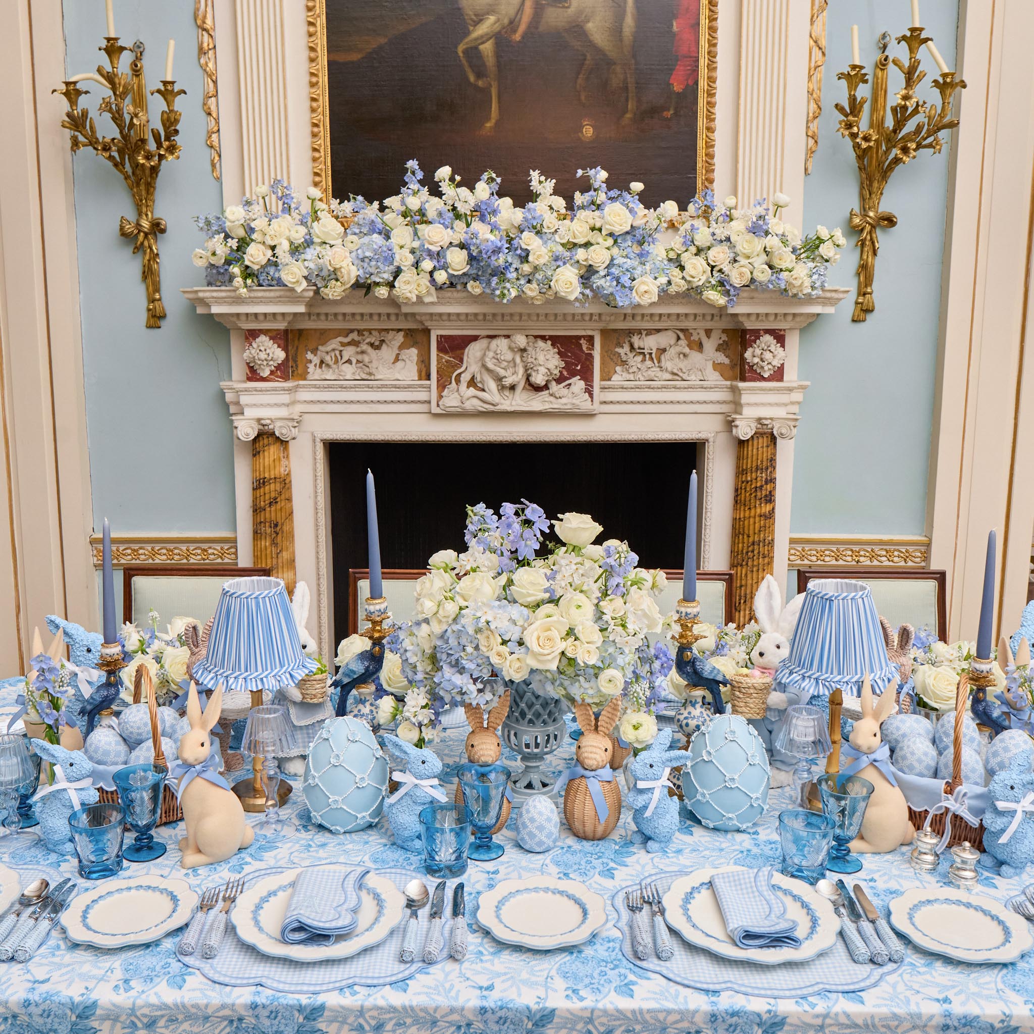Decorative table setting with blue and white floral arrangements, candles, and decorative items in a formal room.