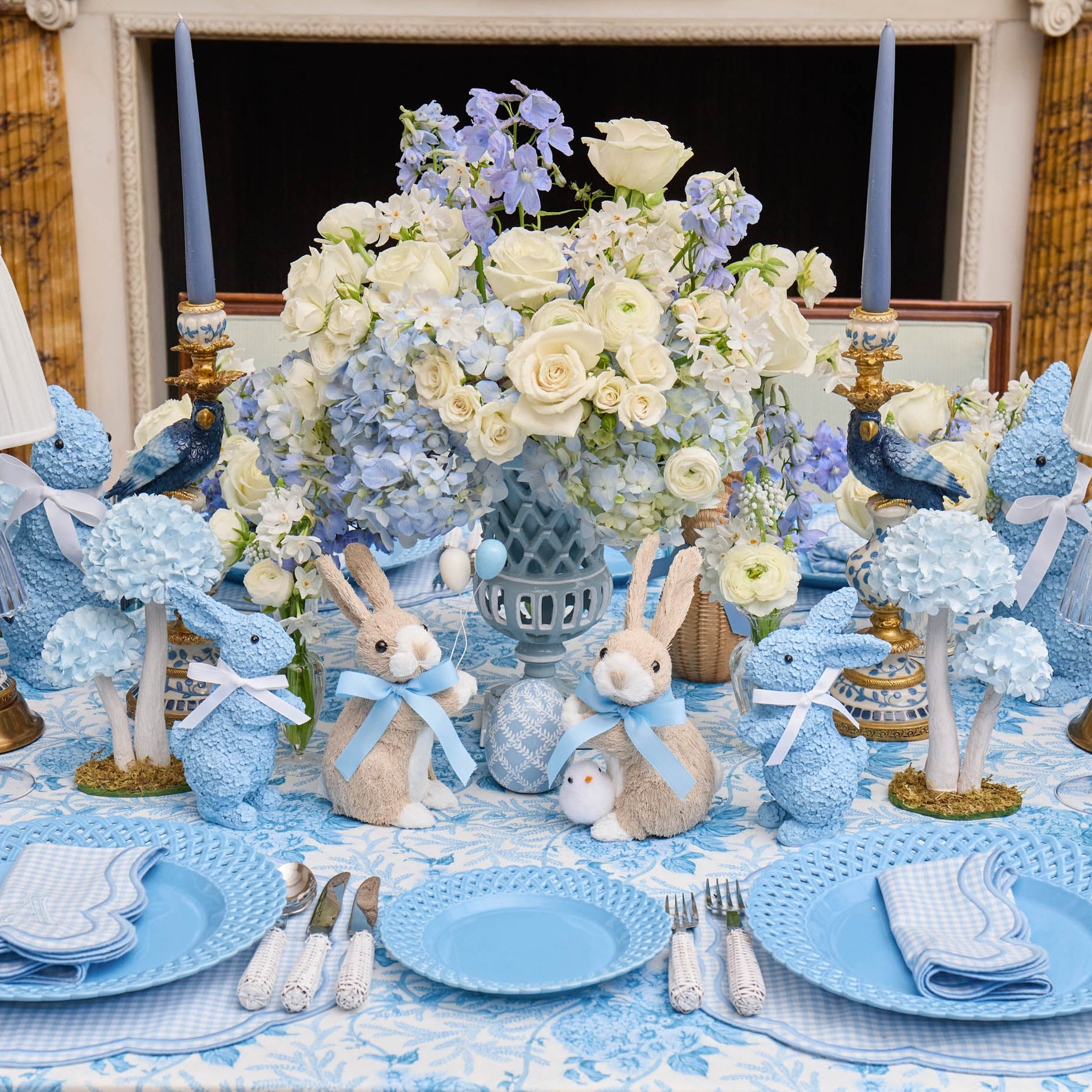 Easter-themed table setting with blue and white decorations, including bunny figurines and floral arrangements.