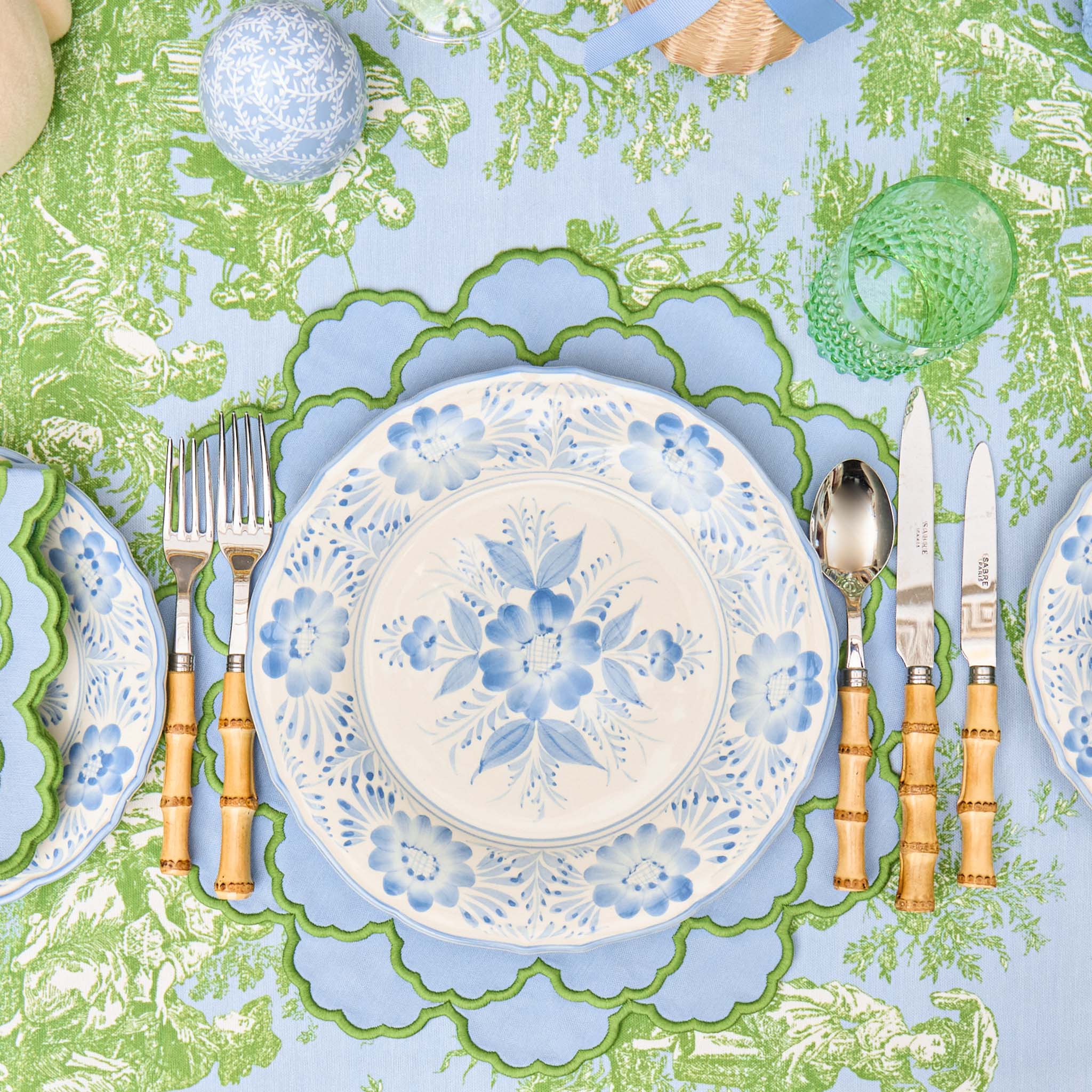 Decorative table setting with floral plates, cutlery, and a patterned tablecloth.