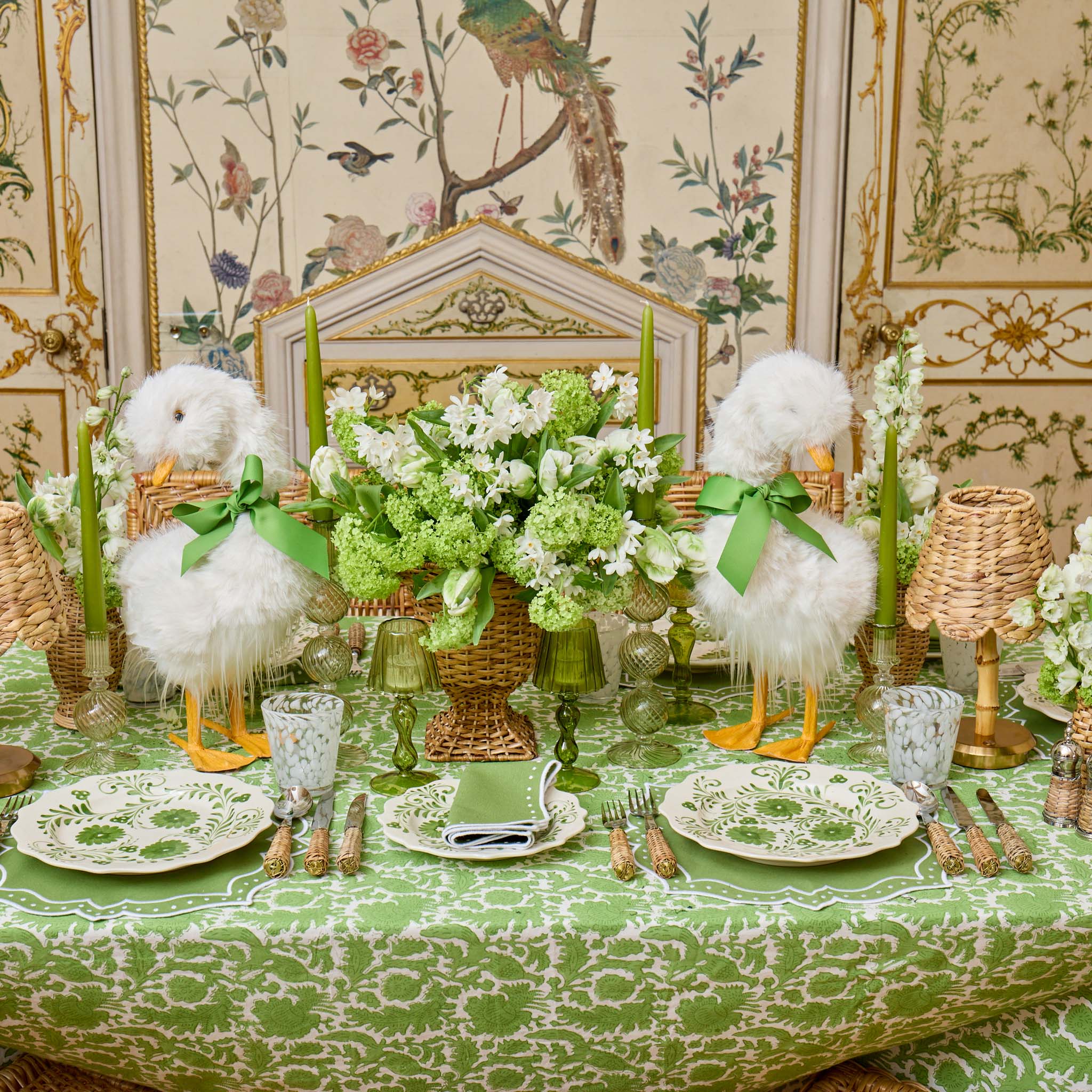 Decorative table setting with white feathers, green ribbons, and floral arrangements in a ornate room.