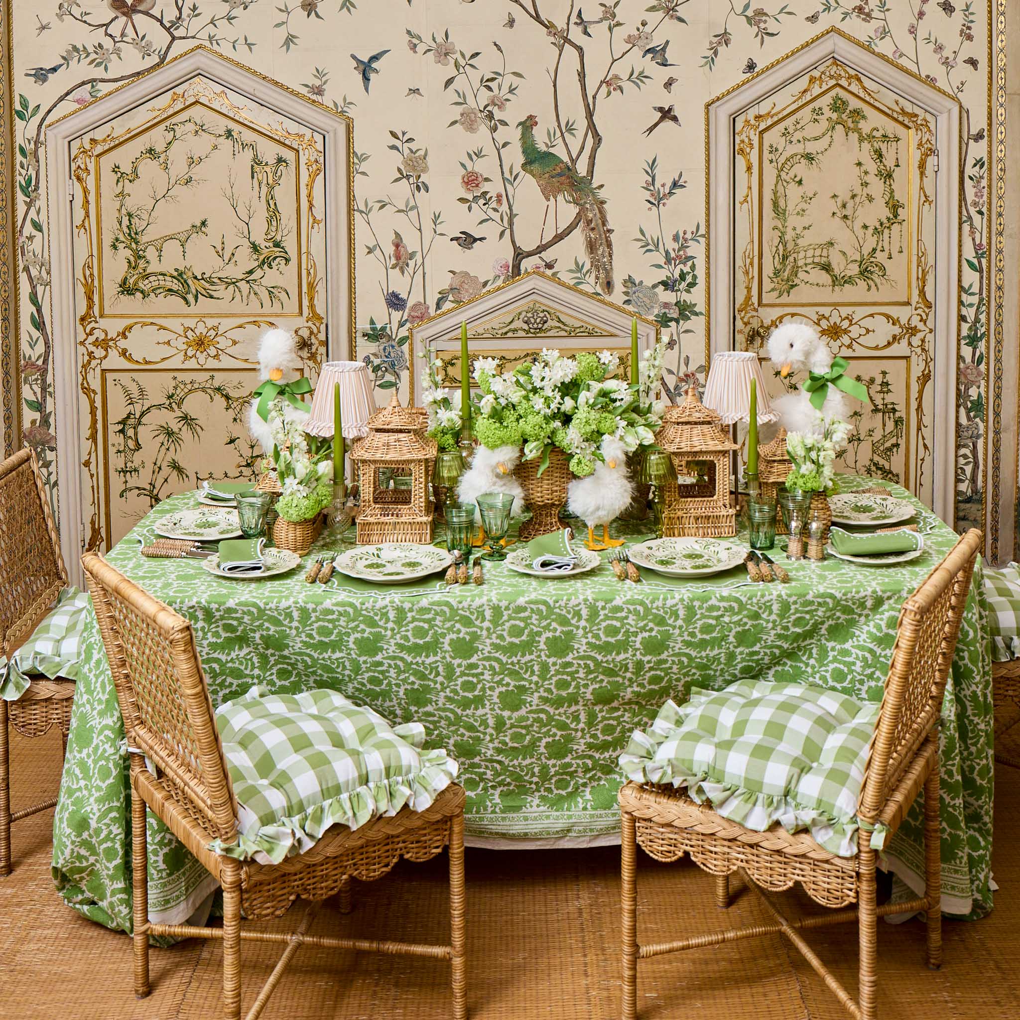Decorative table setting with green tablecloth and floral arrangements in a room with ornate walls.