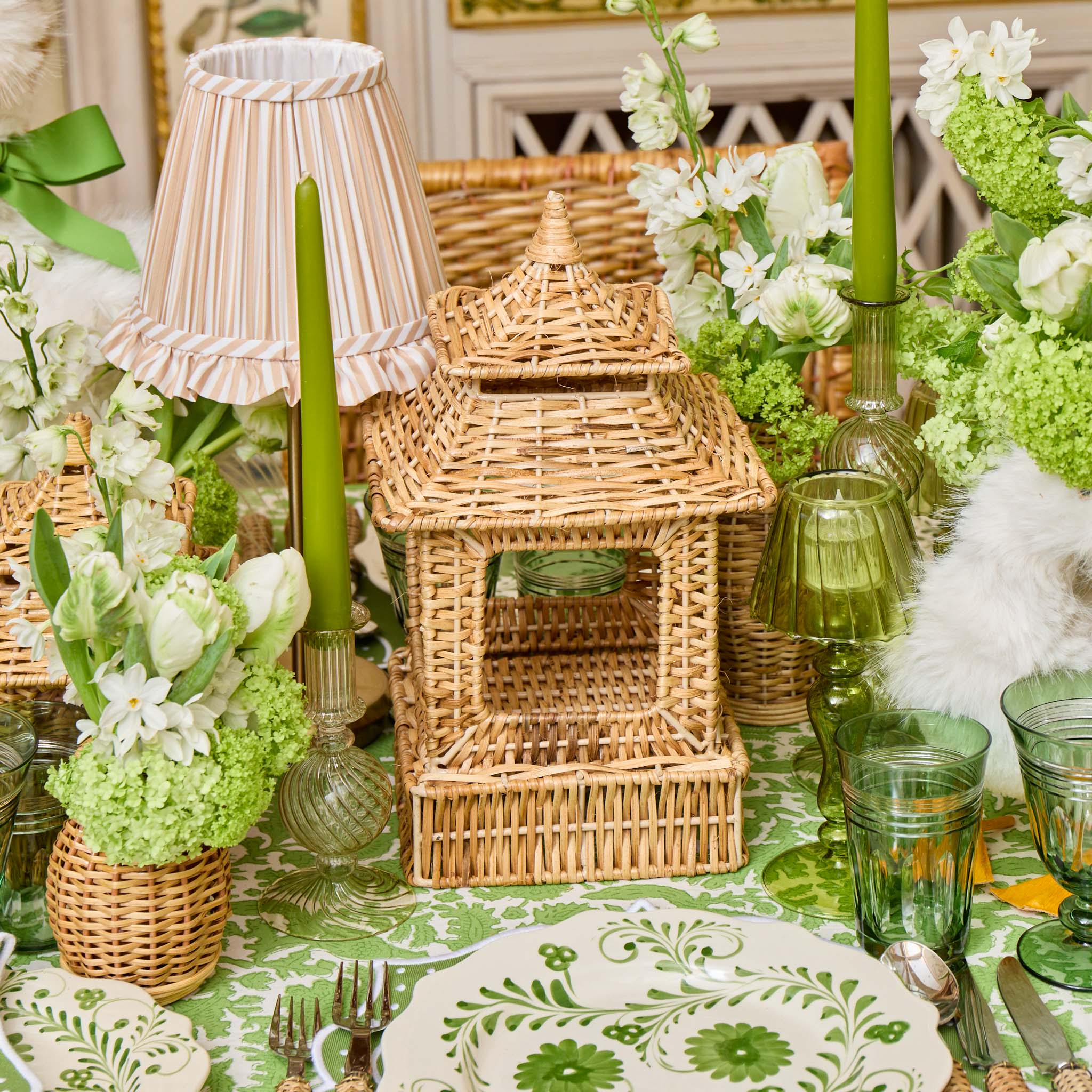 Decorative table setting with wicker birdhouse, green candles, and floral arrangements.