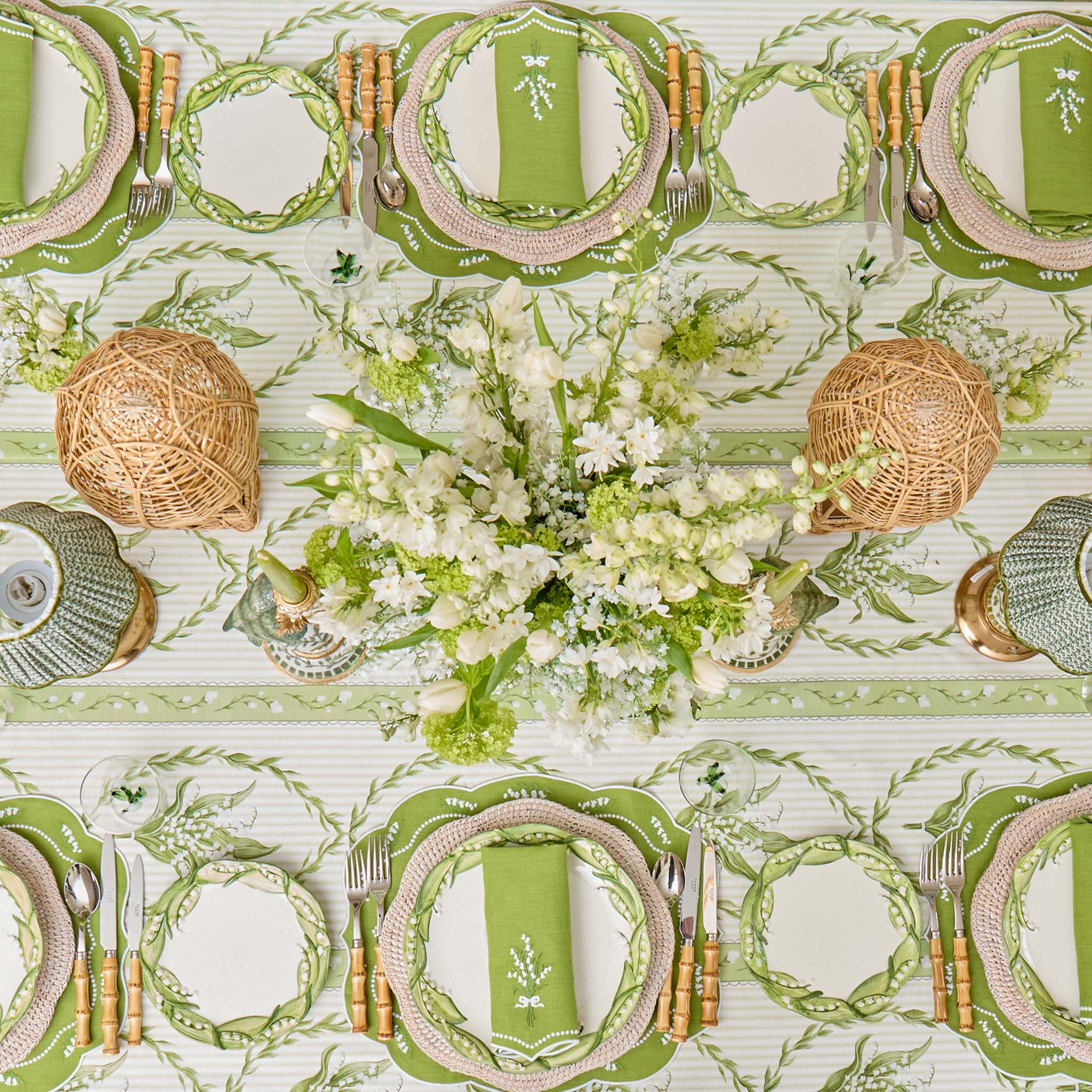 Elegant table setting with green plates, silverware, and a floral centerpiece on a patterned tablecloth.