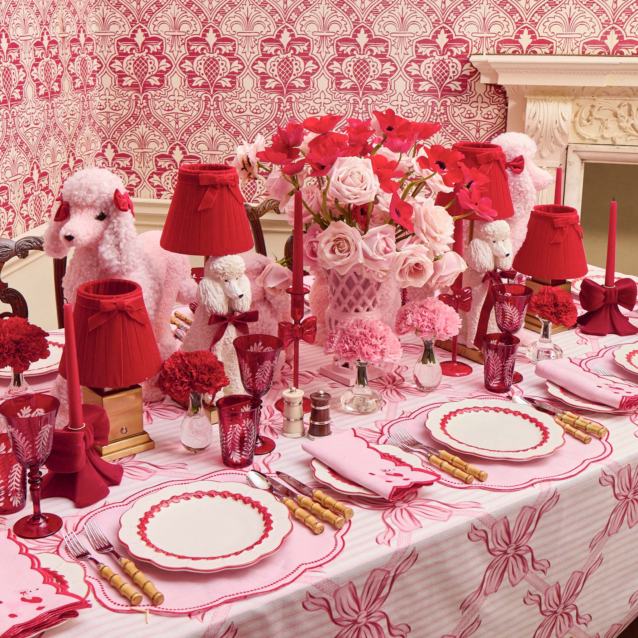 Decorative table setting with red and pink elements, including flowers and tableware, against a patterned wallpaper background.
