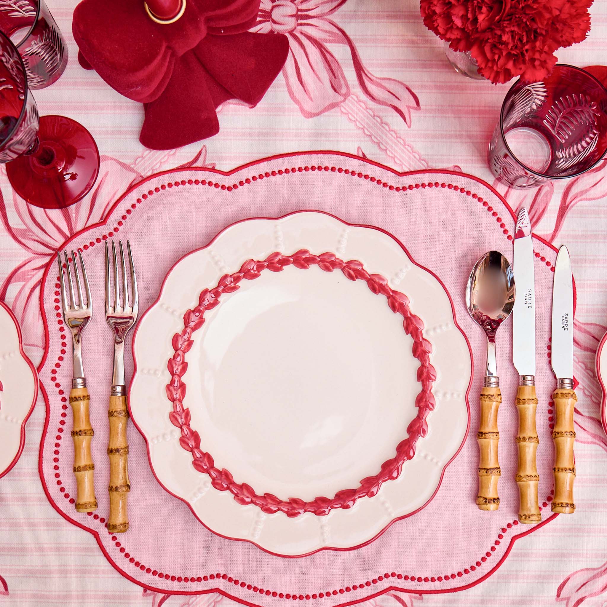 Elegant table setting with red and white plates, cutlery, and decorative elements on a pink tablecloth.