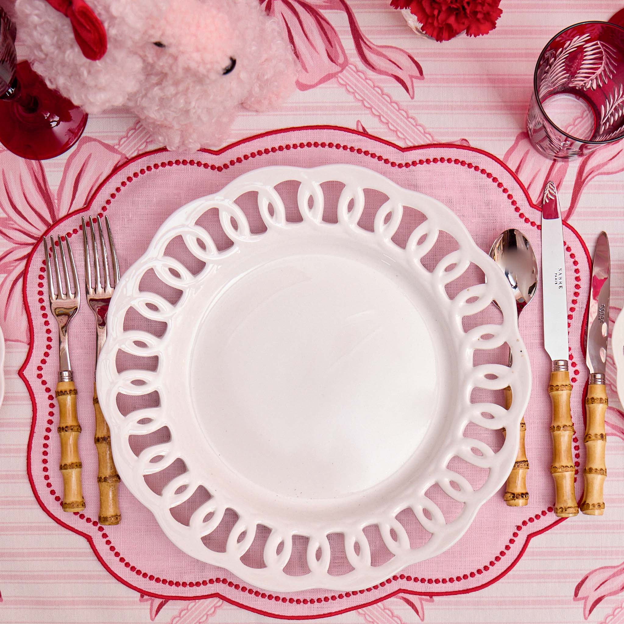 Dinner table setting with a decorative plate, cutlery, and pink tablecloth.