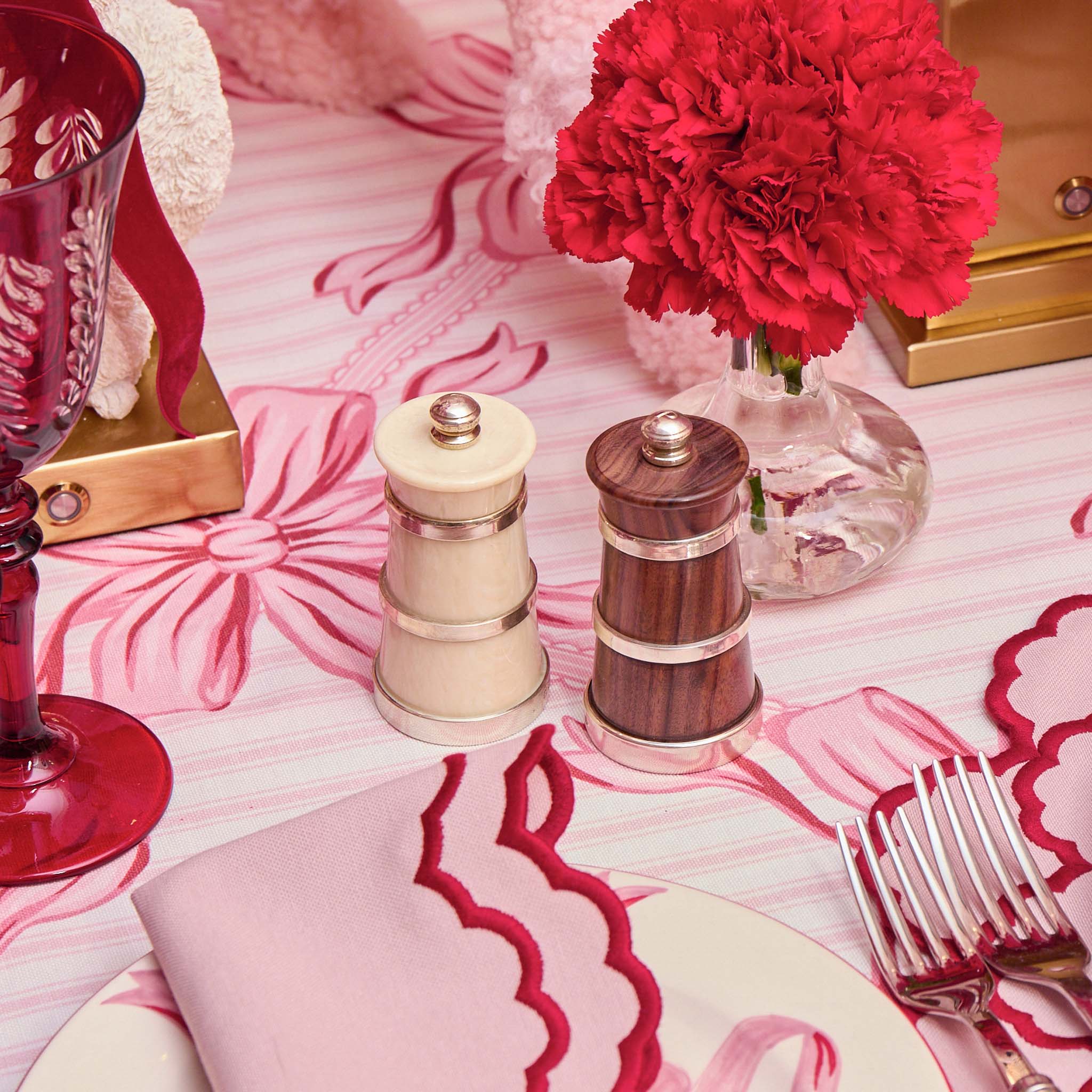 Decorative table setting with pink floral tablecloth, red glass, wooden salt and pepper shakers, and silverware.