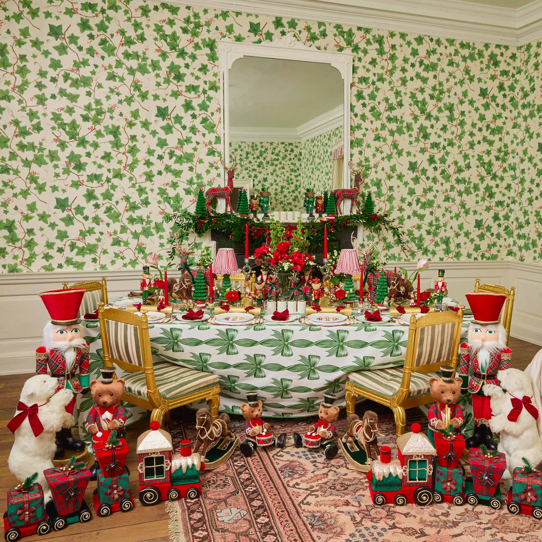 Decorative Christmas scene with teddy bears, trains, and a table set against a patterned wall.