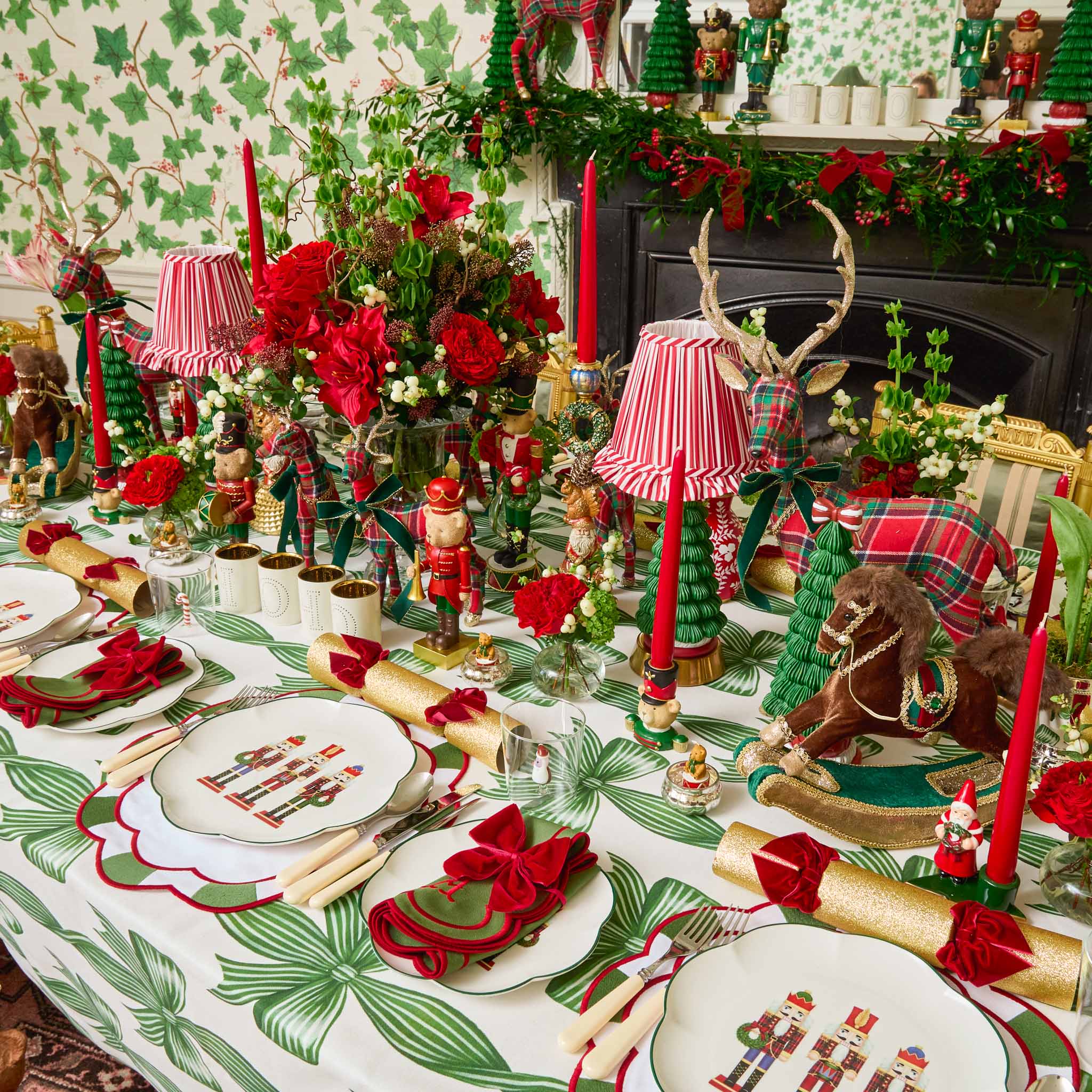 Decorative Christmas table setting with red and green accents, including candles, flowers, and small figurines.