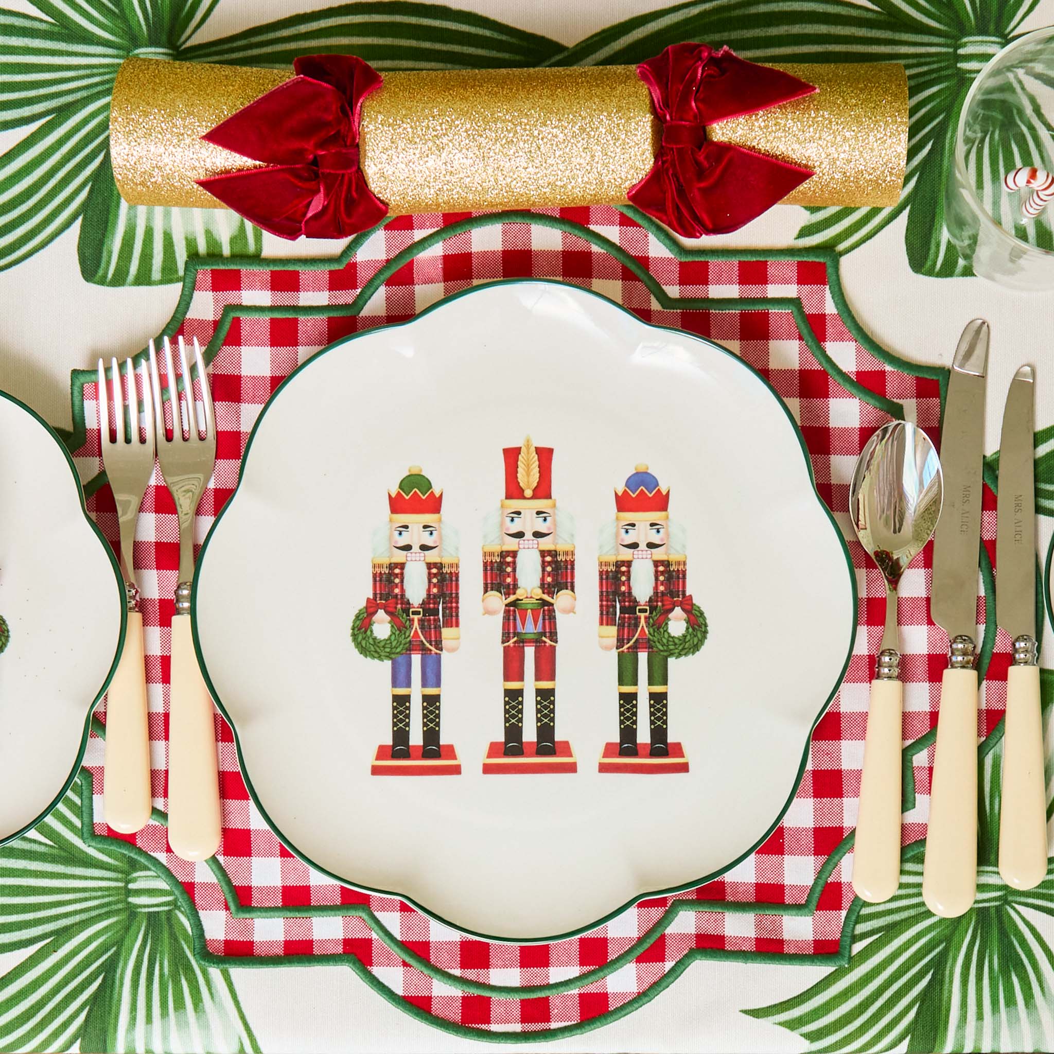 Christmas-themed table setting with nutcracker design plate, plaid placemat, and festive cutlery.