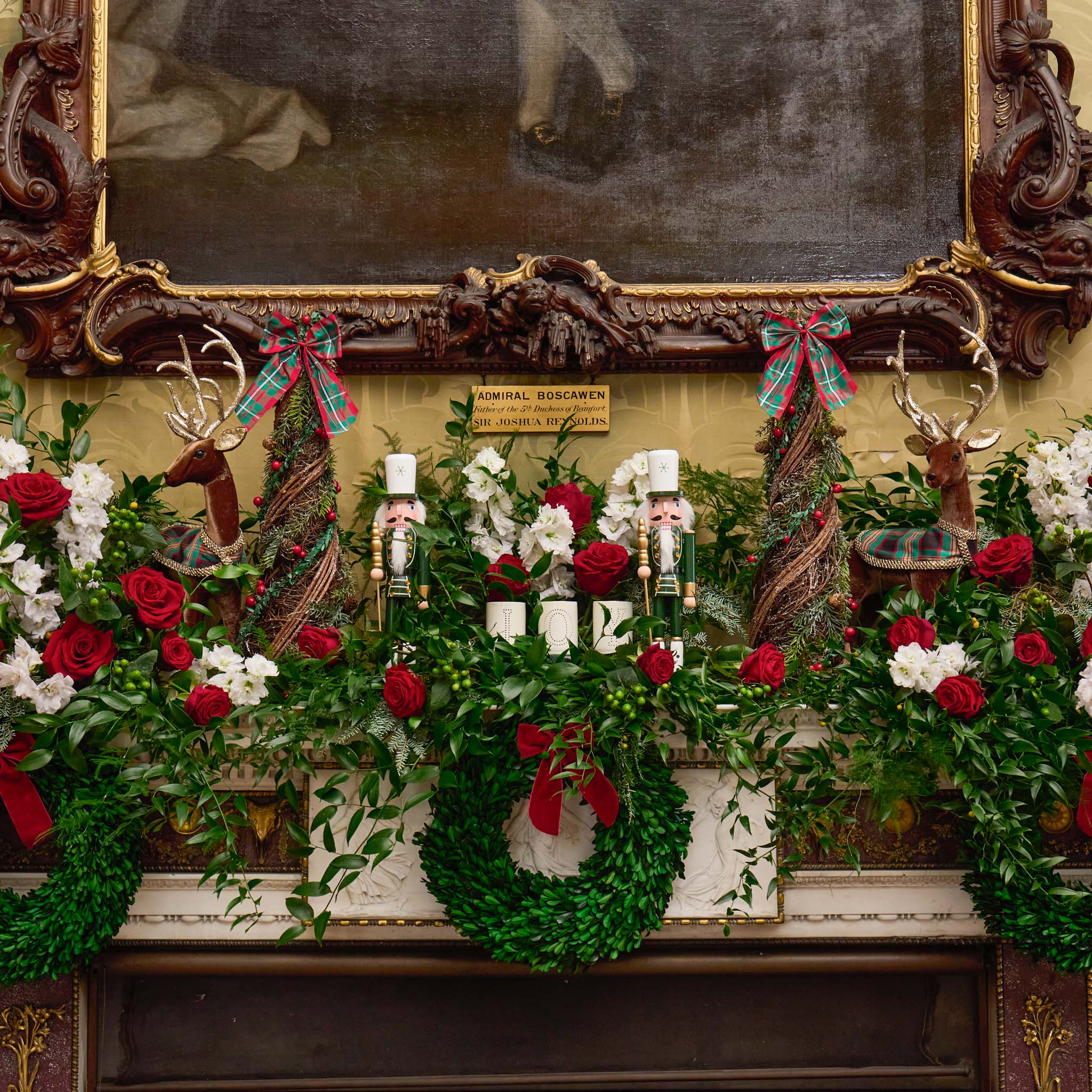 Decorative Christmas mantel with wreaths, flowers, and ornaments in front of a mirror.