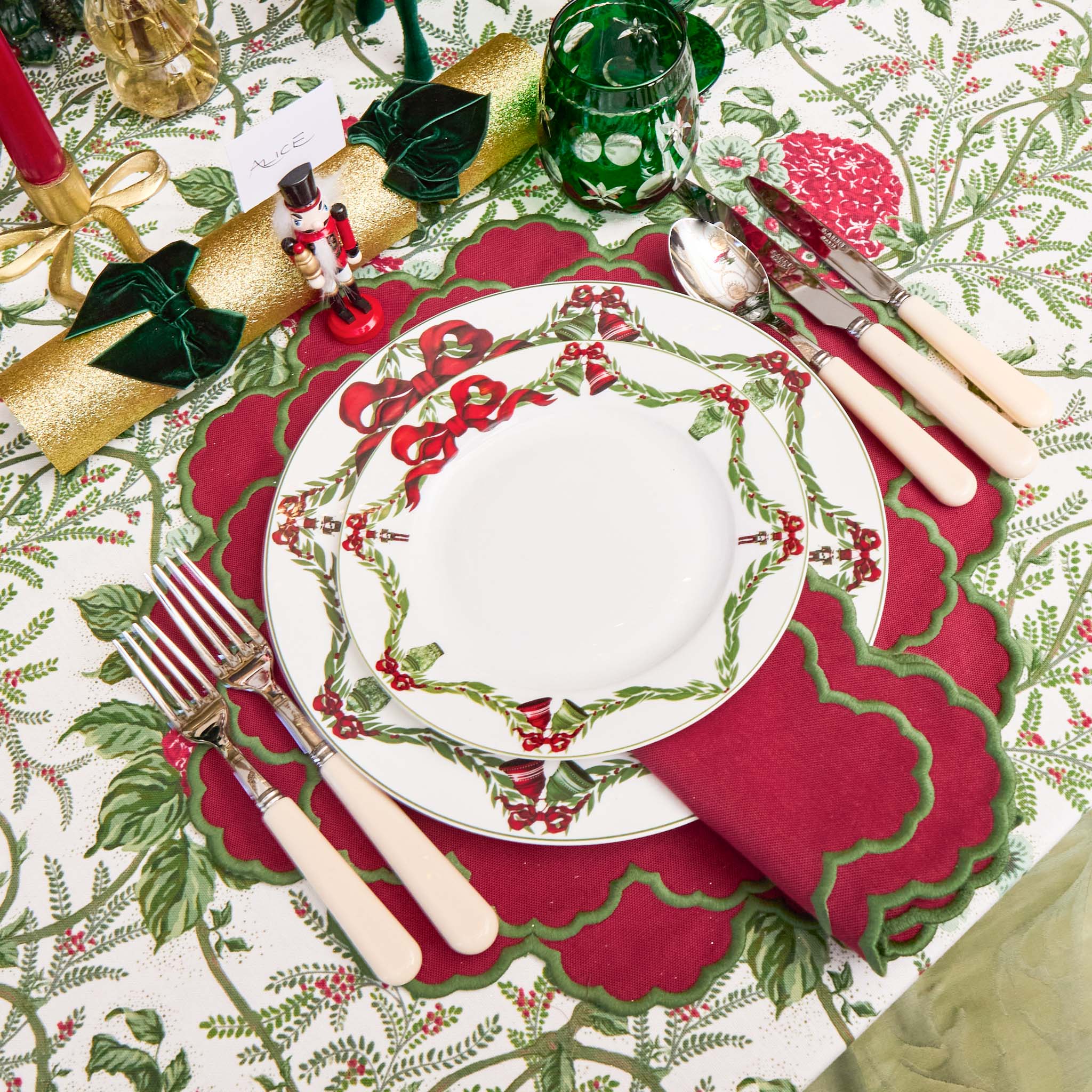 Christmas table setting with decorative plates, cutlery, and napkins on a patterned tablecloth.