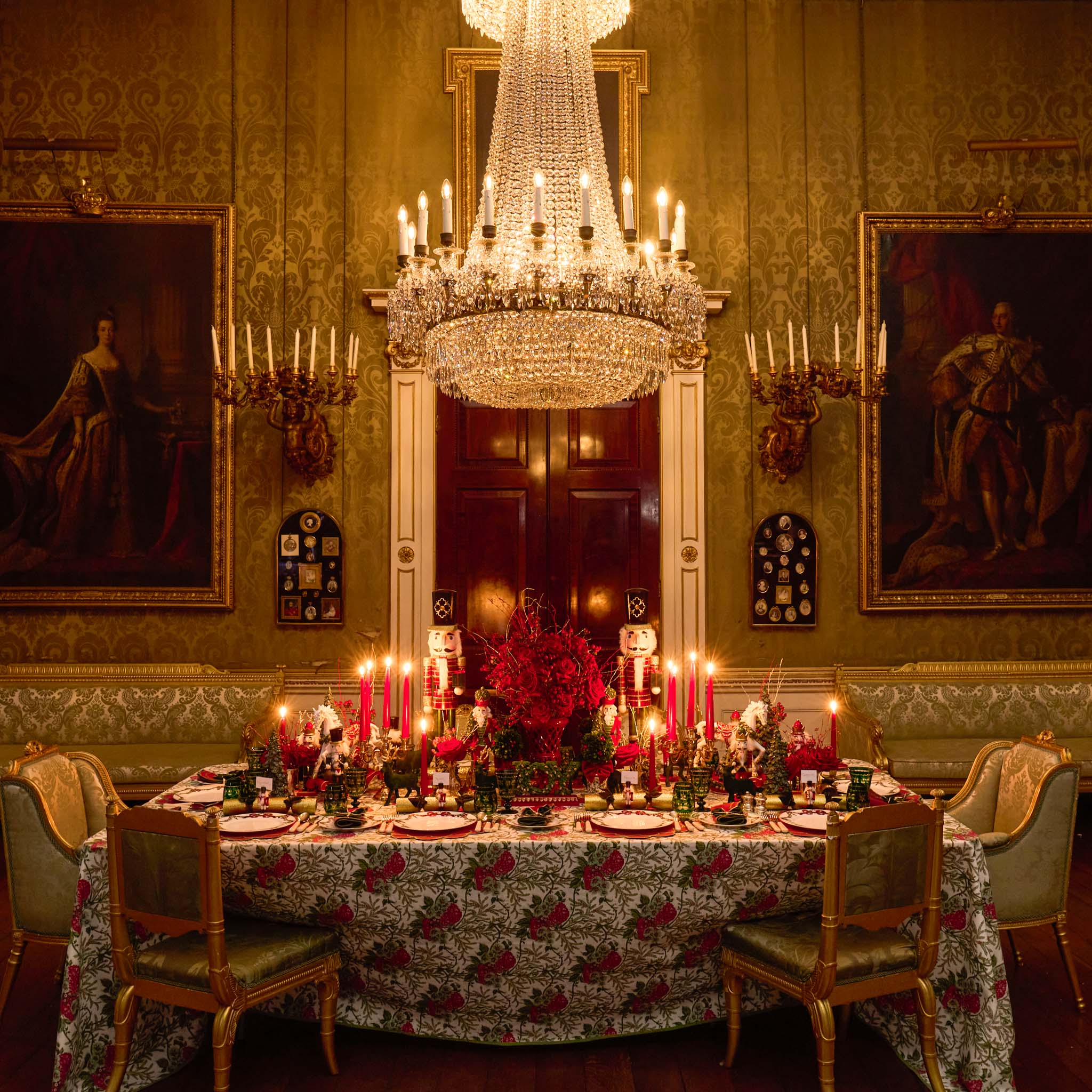 Dining room with ornate table setting, chandelier, and classical portraits on the walls.