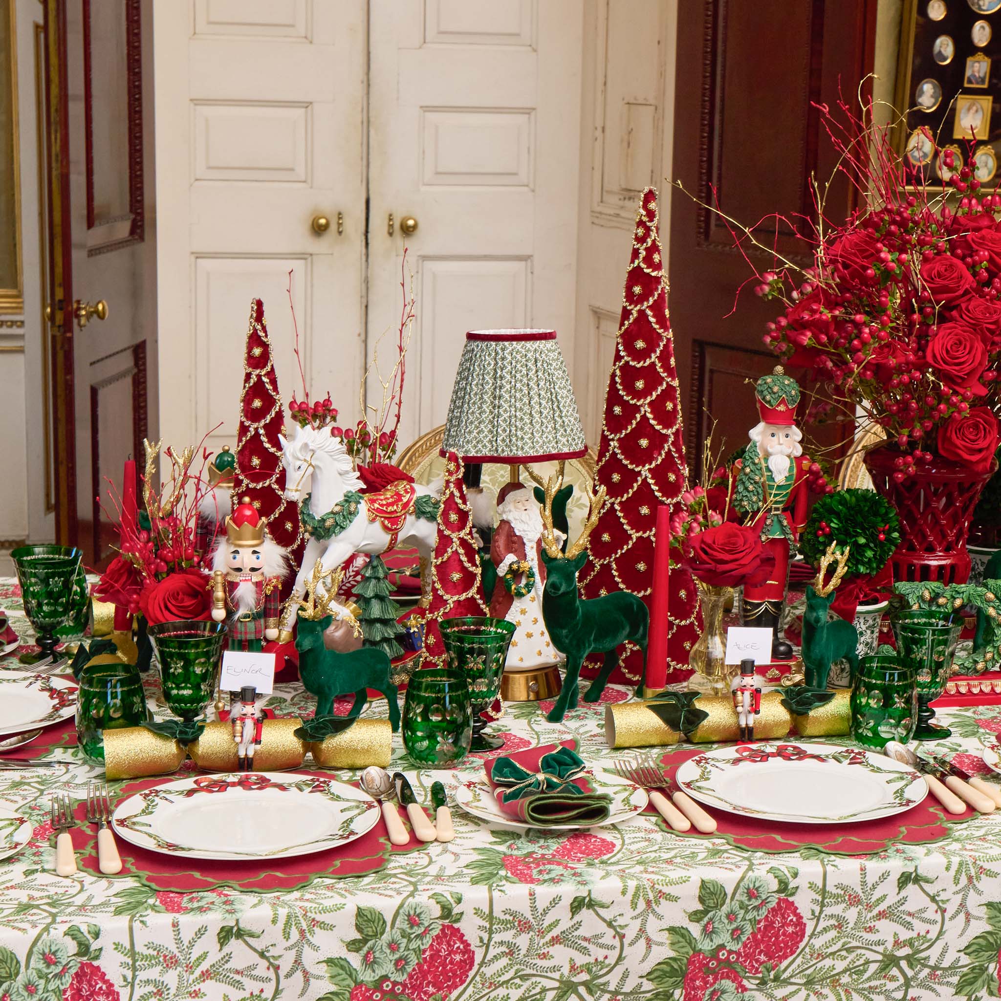 Decorative Christmas table setting with red and green ornaments, tableware, and floral arrangements.