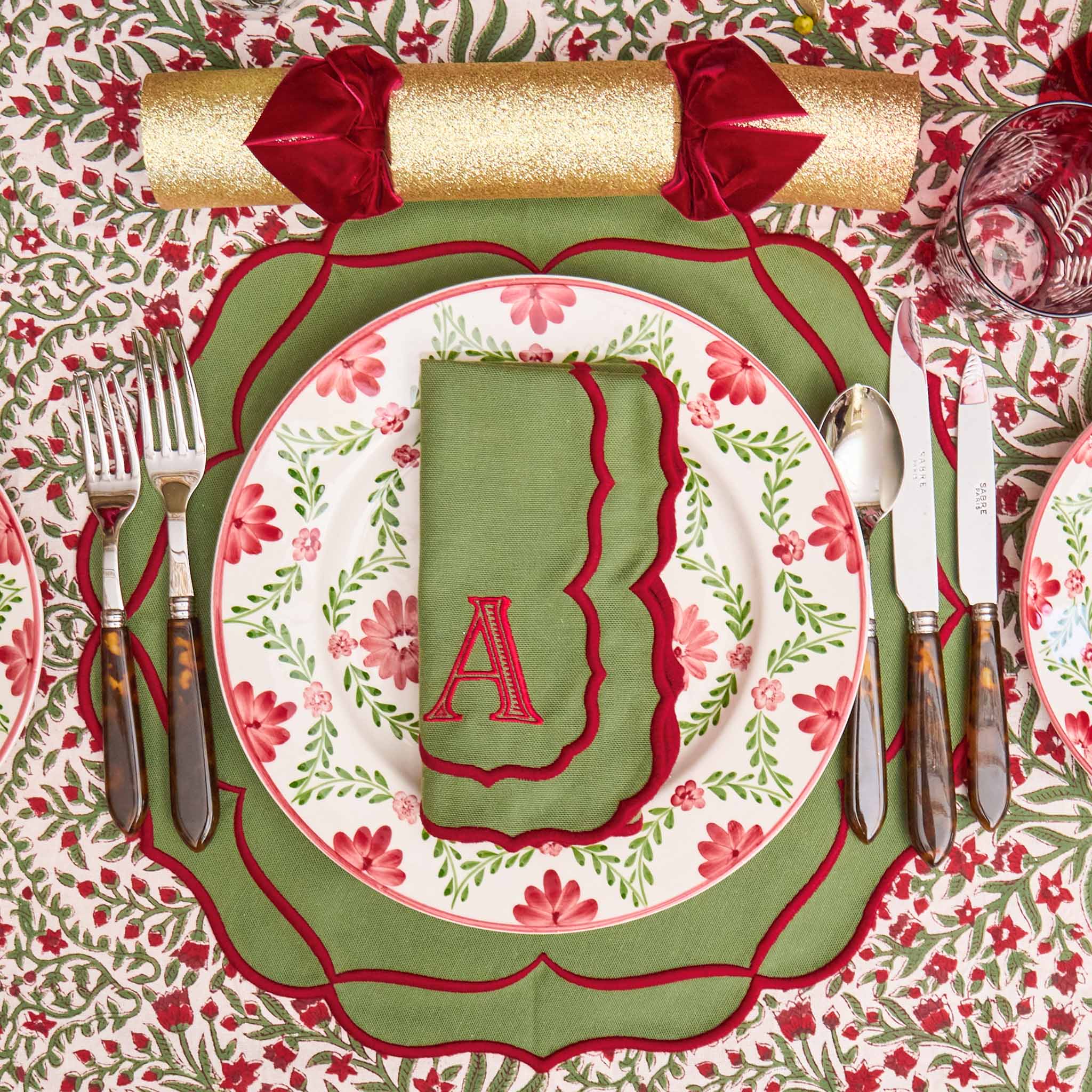 Decorative table setting with floral plates, cutlery, and a napkin on a patterned tablecloth.