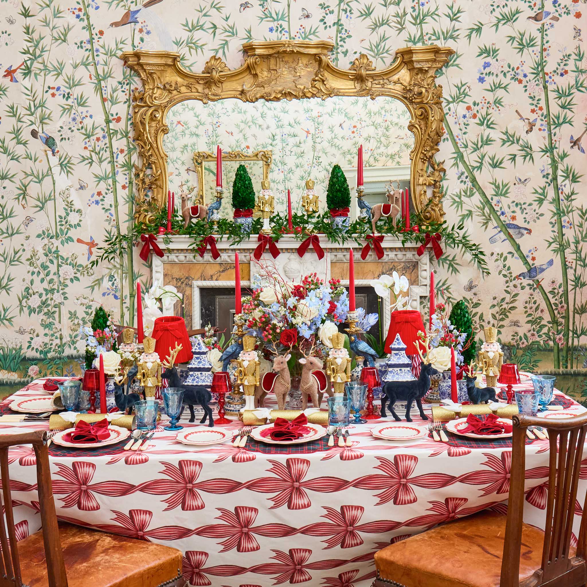 Decorative table setting with floral arrangements and red ribbons in a room with ornate wallpaper and a large mirror.