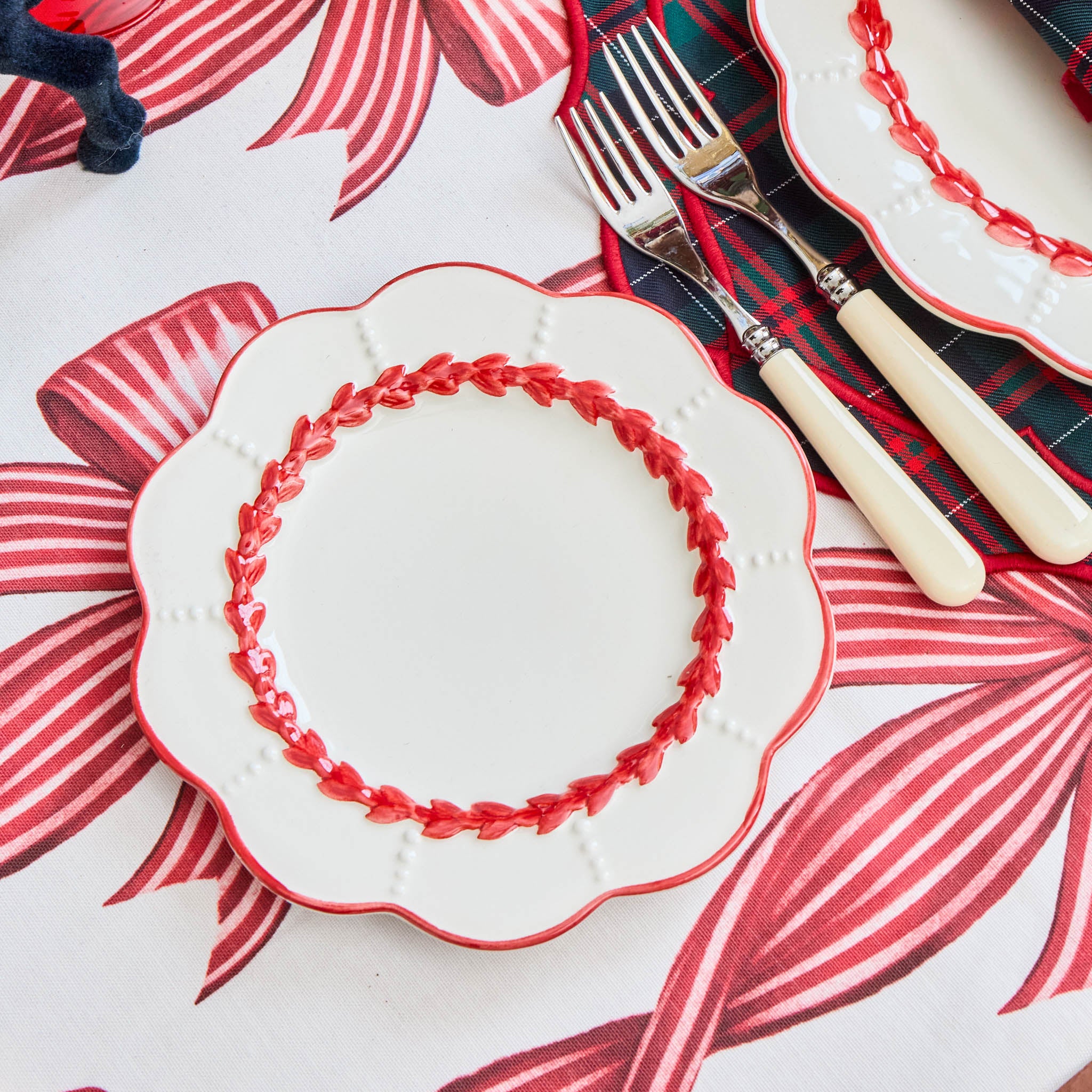 Decorative plate with red rim on a floral tablecloth with cutlery.