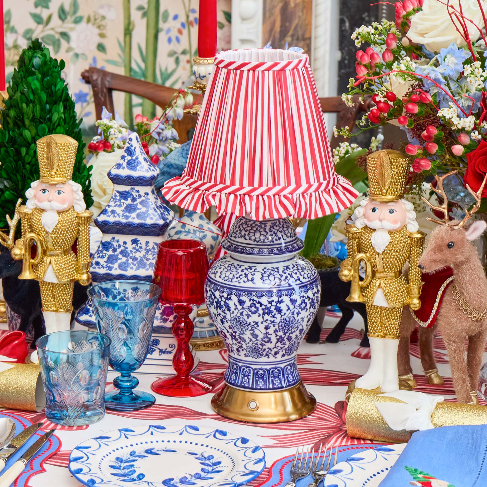 Decorative table setting with blue and white lamp, nutcrackers, and floral arrangements.