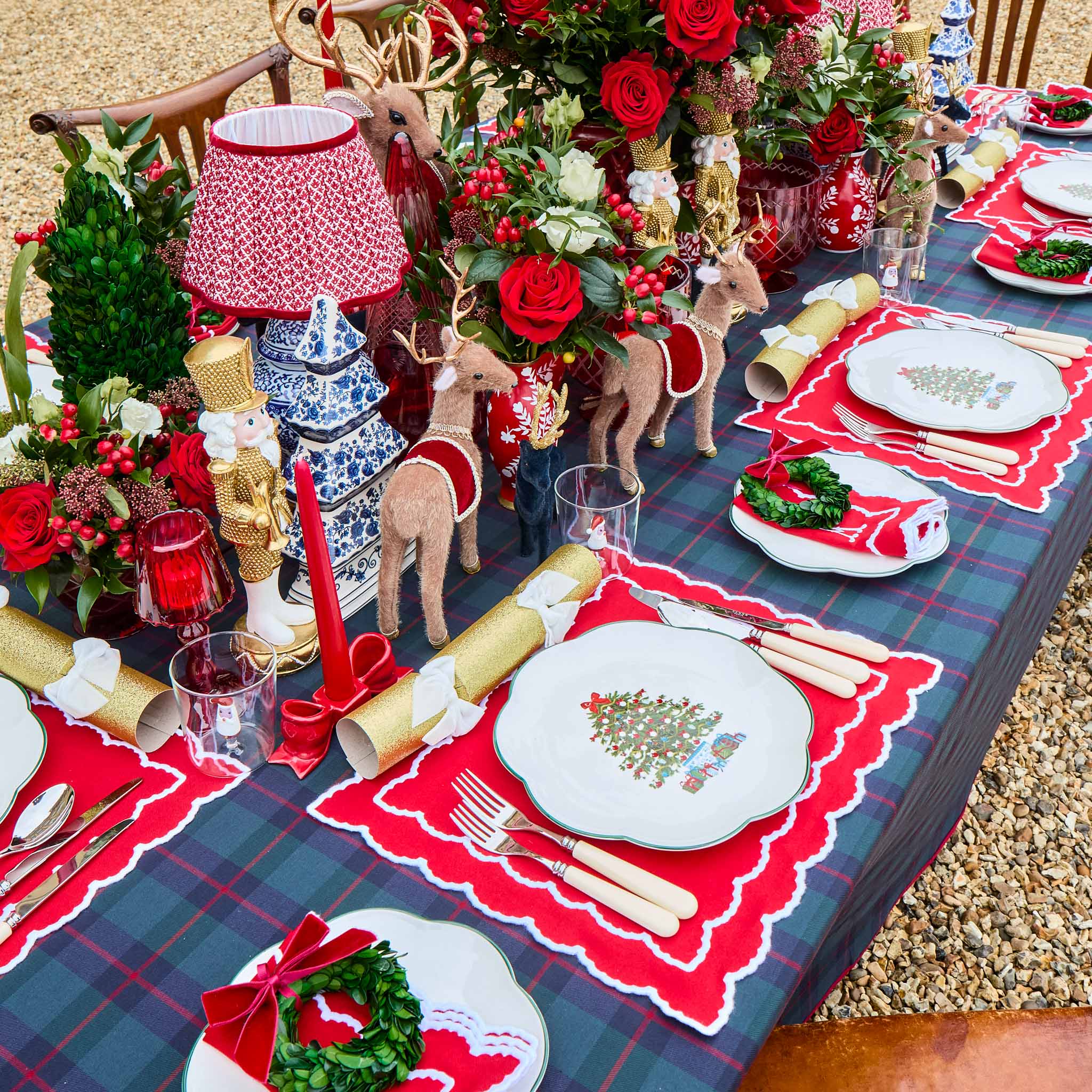 Decorative Christmas table setting with red and green accents, including place settings and floral arrangements.