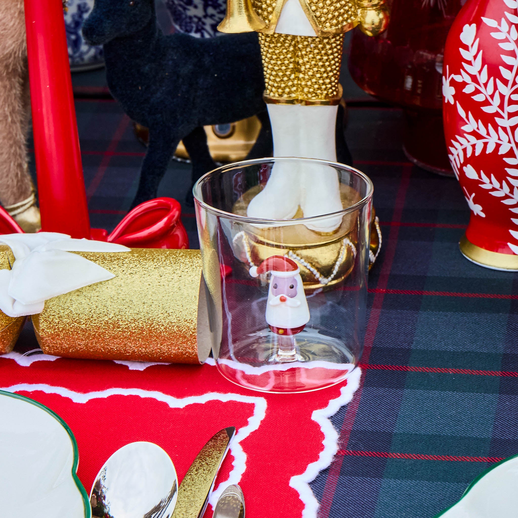 Decorative glass with a small Santa Claus figure on a tablecloth with Christmas decorations.