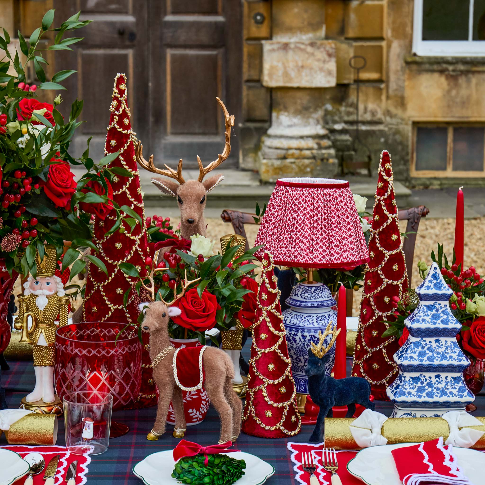 Decorative Christmas table setting with trees, deer figurines, and candles in front of a stone building.