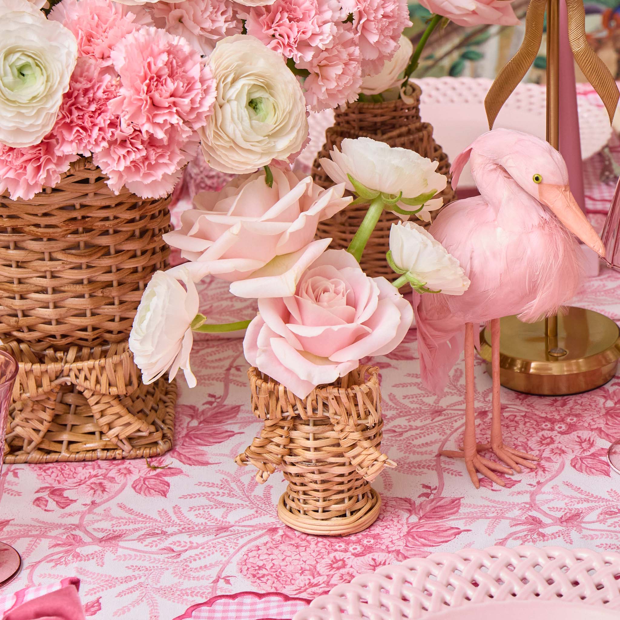 Decorative setting with pink flowers, wicker baskets, and a pink flamingo on a floral tablecloth.