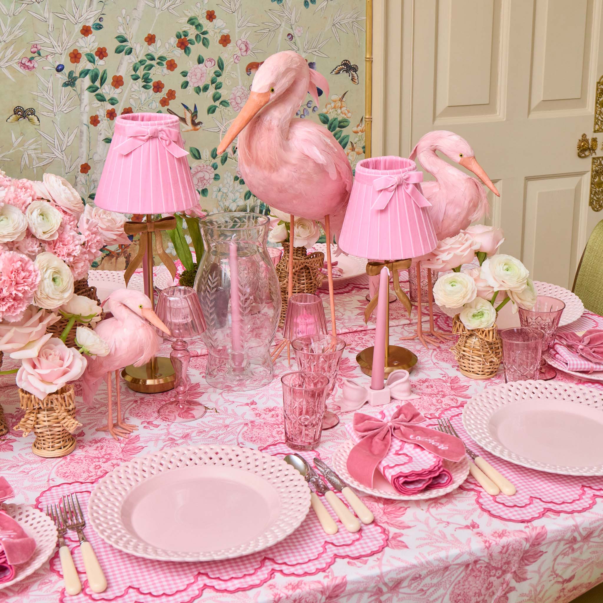 Pink flamingo-themed table setting with floral arrangements and decorative lamps.