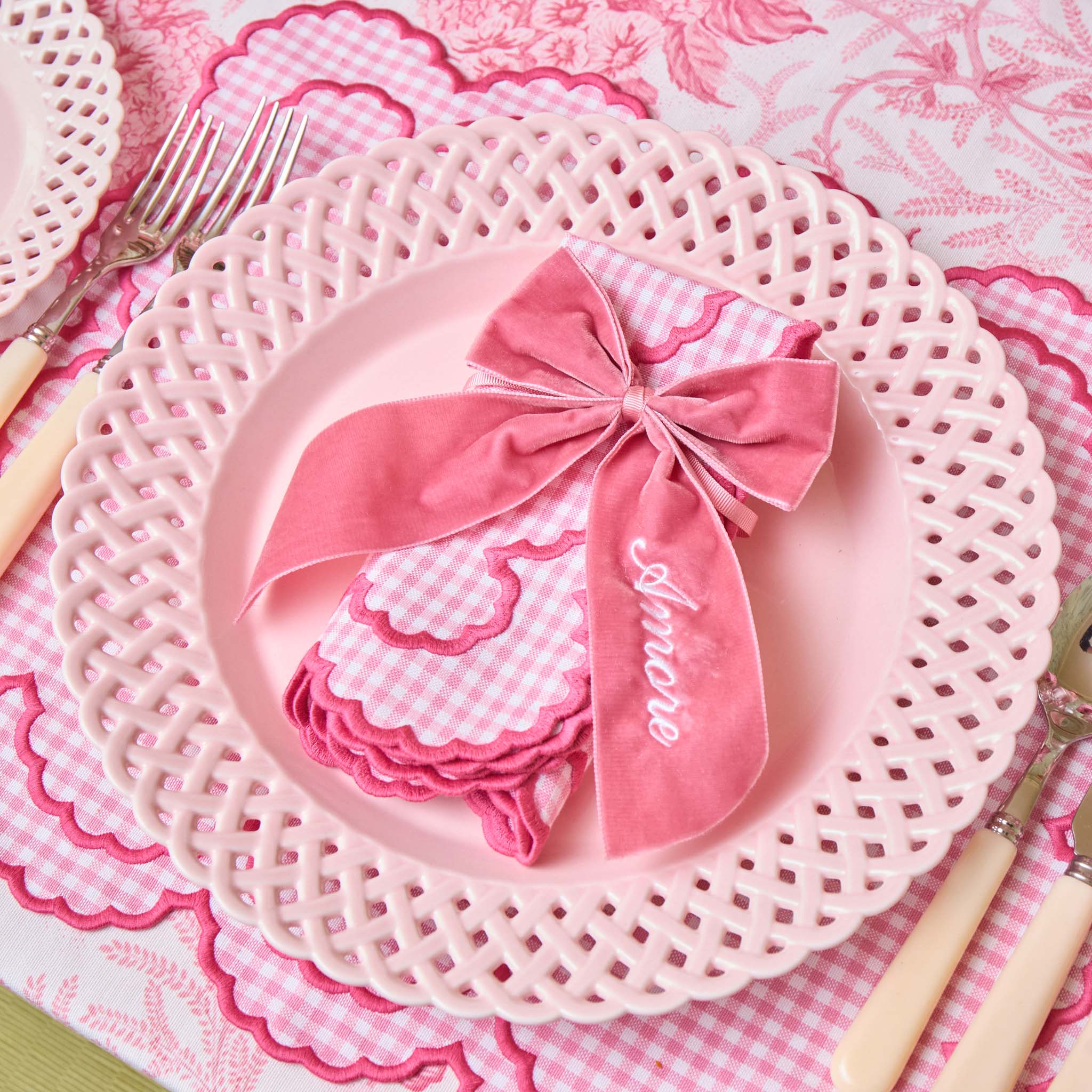 Pink plate with decorative napkin and lace doily on a matching pink and white checkered tablecloth.