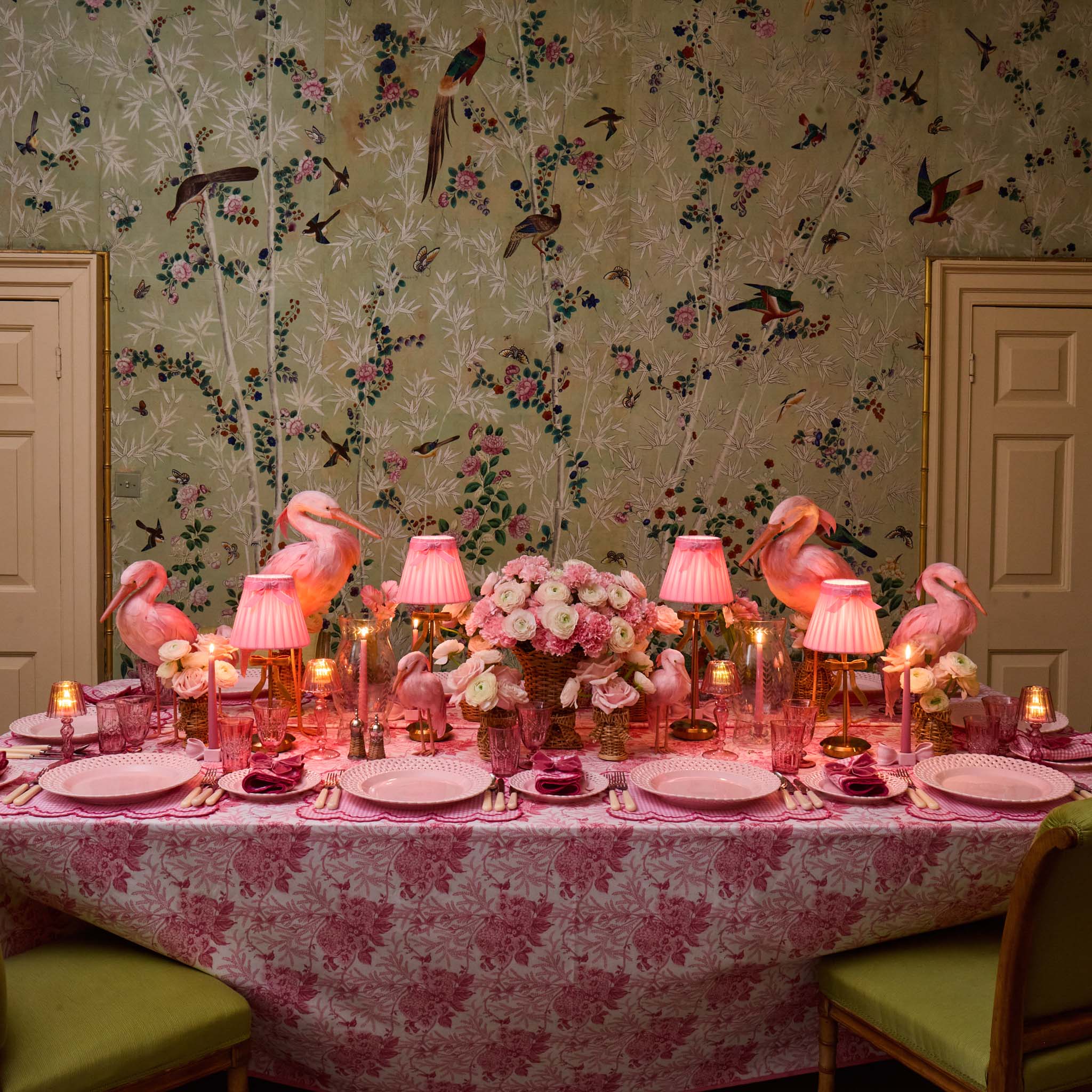 Decorative table setting with flamingo decorations against a floral wallpapered wall.