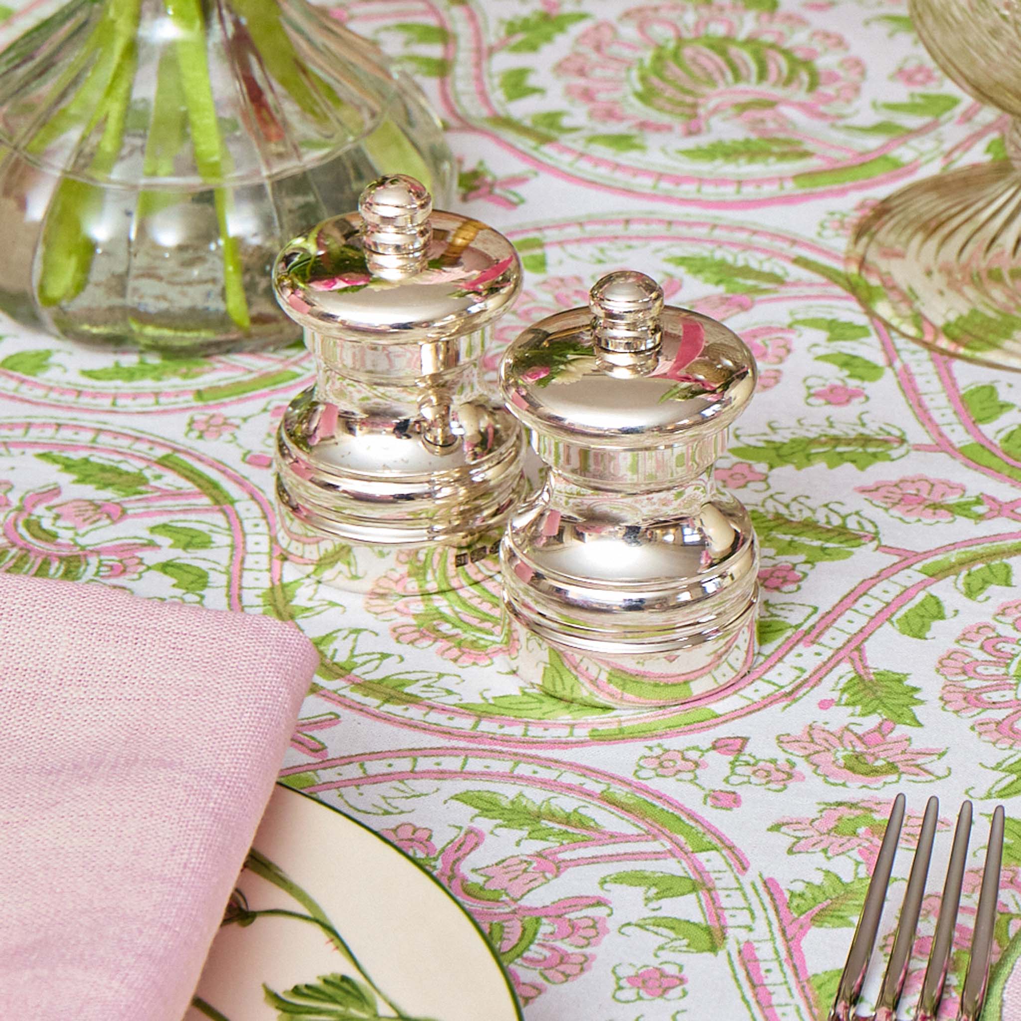Silver salt and pepper shakers on a patterned tablecloth with pink and green design.