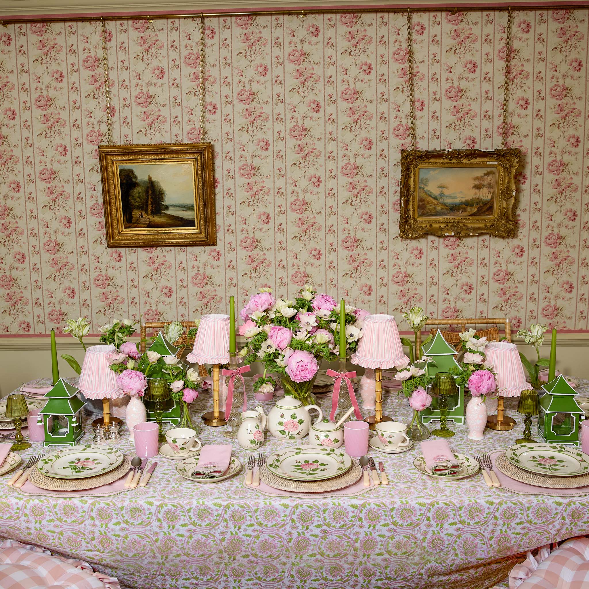 Decorative table setting with floral arrangements and tableware against a floral wallpapered wall.