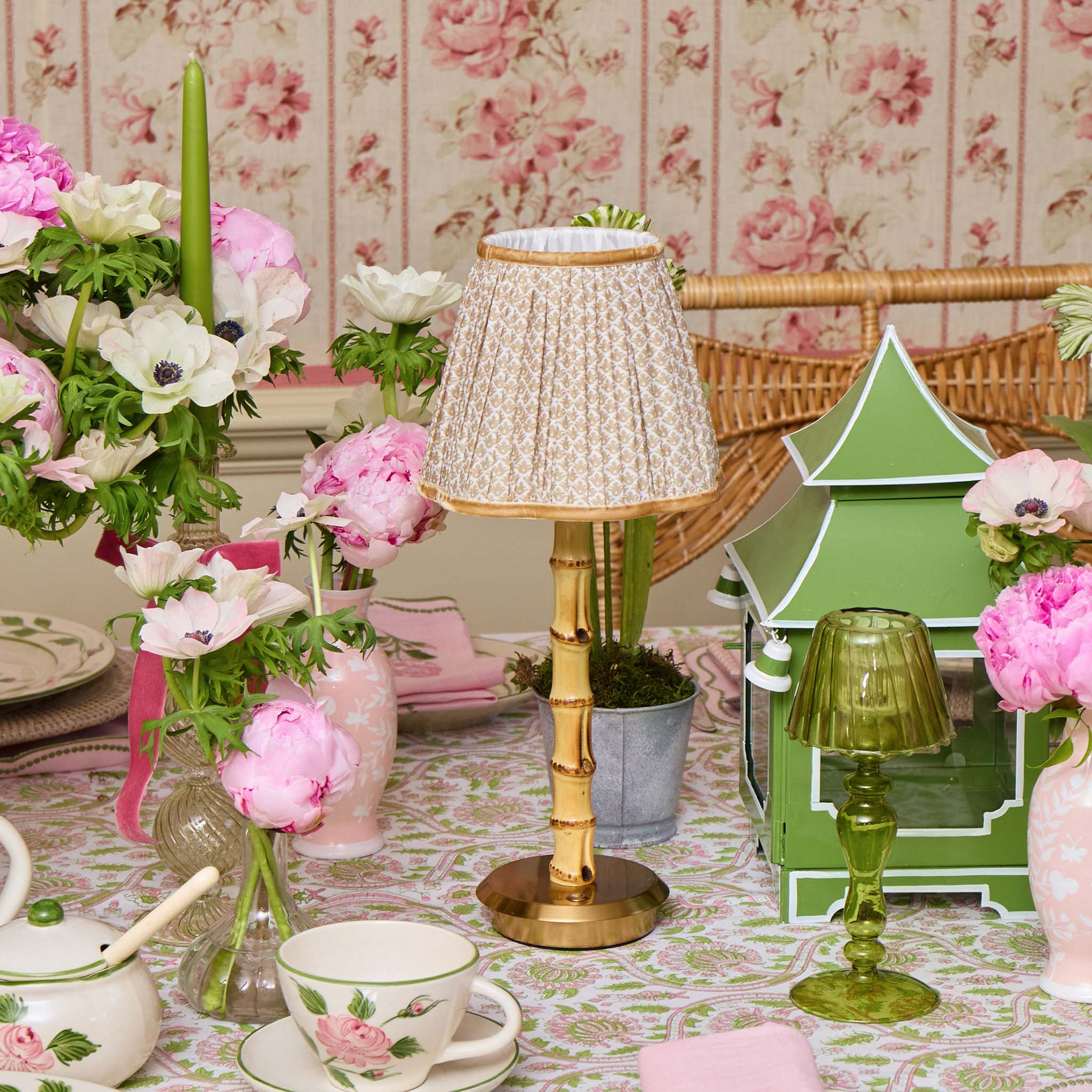 Decorative table setting with floral arrangements, a gold lamp, and a green tree-shaped object against a floral wallpaper background.