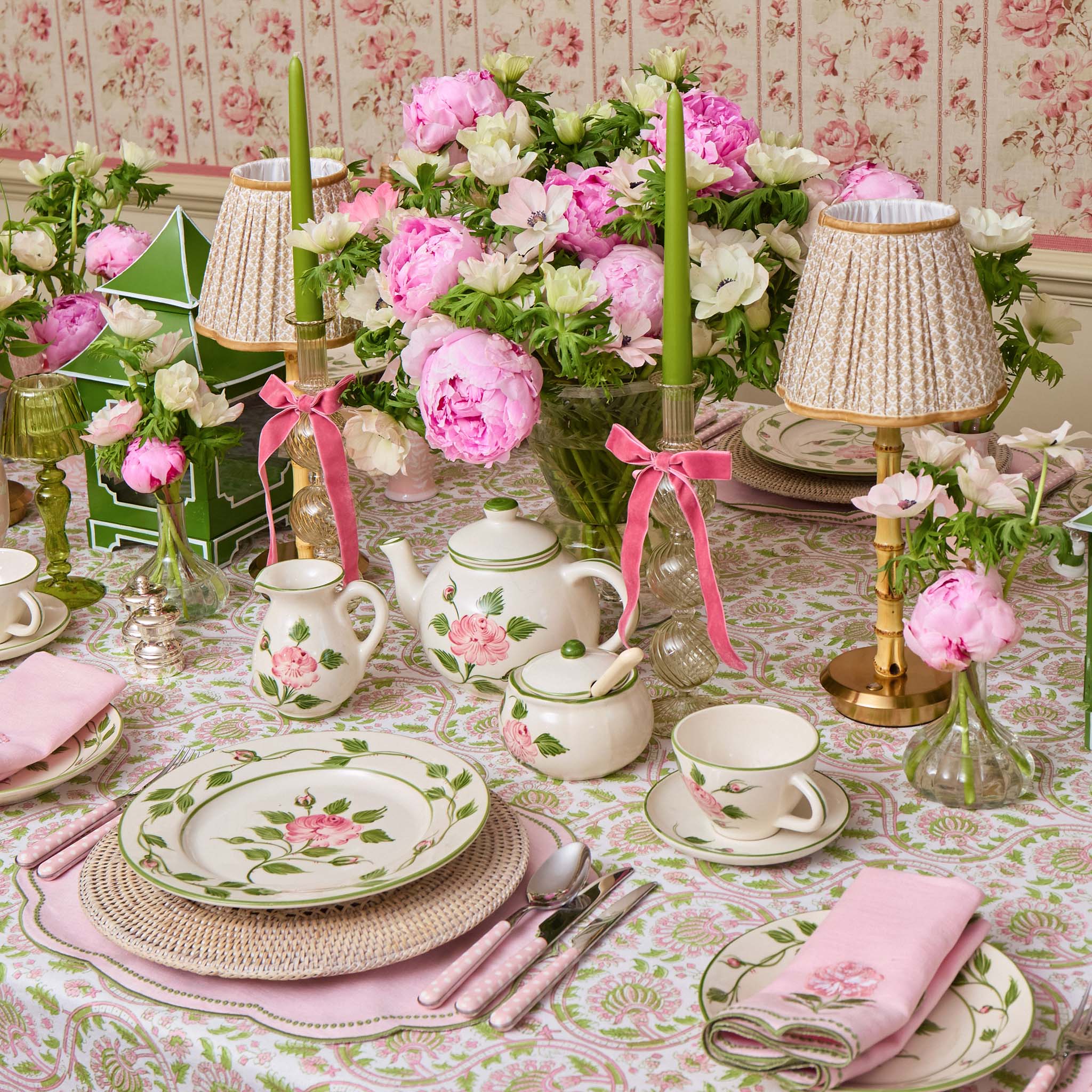 Elegant table setting with floral china, pink napkins, and decorative candles on a patterned tablecloth.